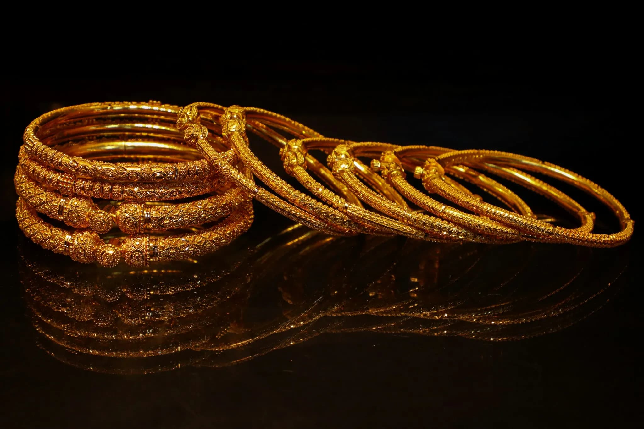 A stack of ornate gold bangles on a dark surface