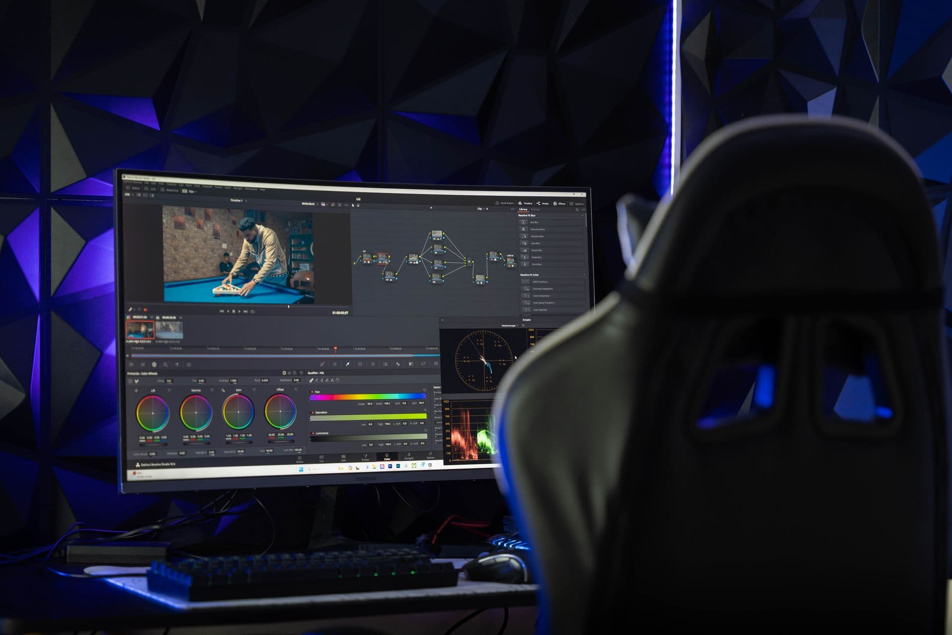 Curved monitor showing colour grading software in a dark edit suite with blue and purple lights