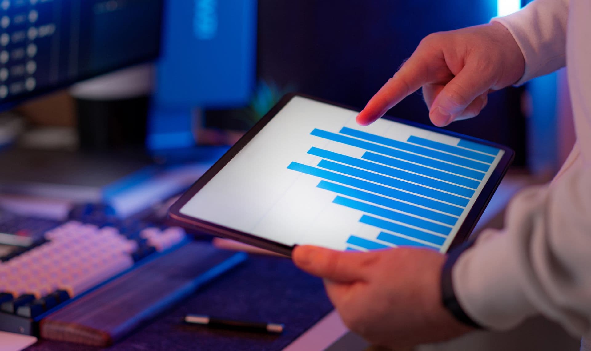 Hands holding a tablet showing a blue bar chart, with a finger pointing at the data