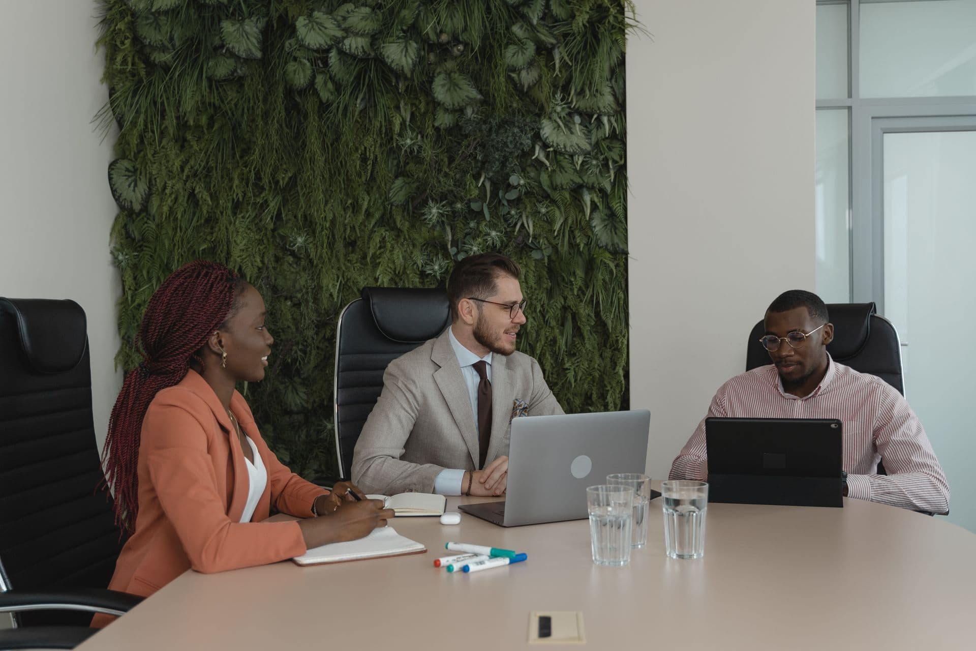 Three colleagues meeting at a conference table in front of a green living plant wall