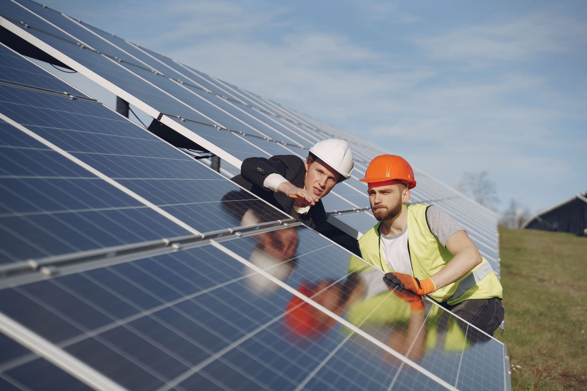 Two workers in hard hats inspecting rows of solar panels at a solar installation