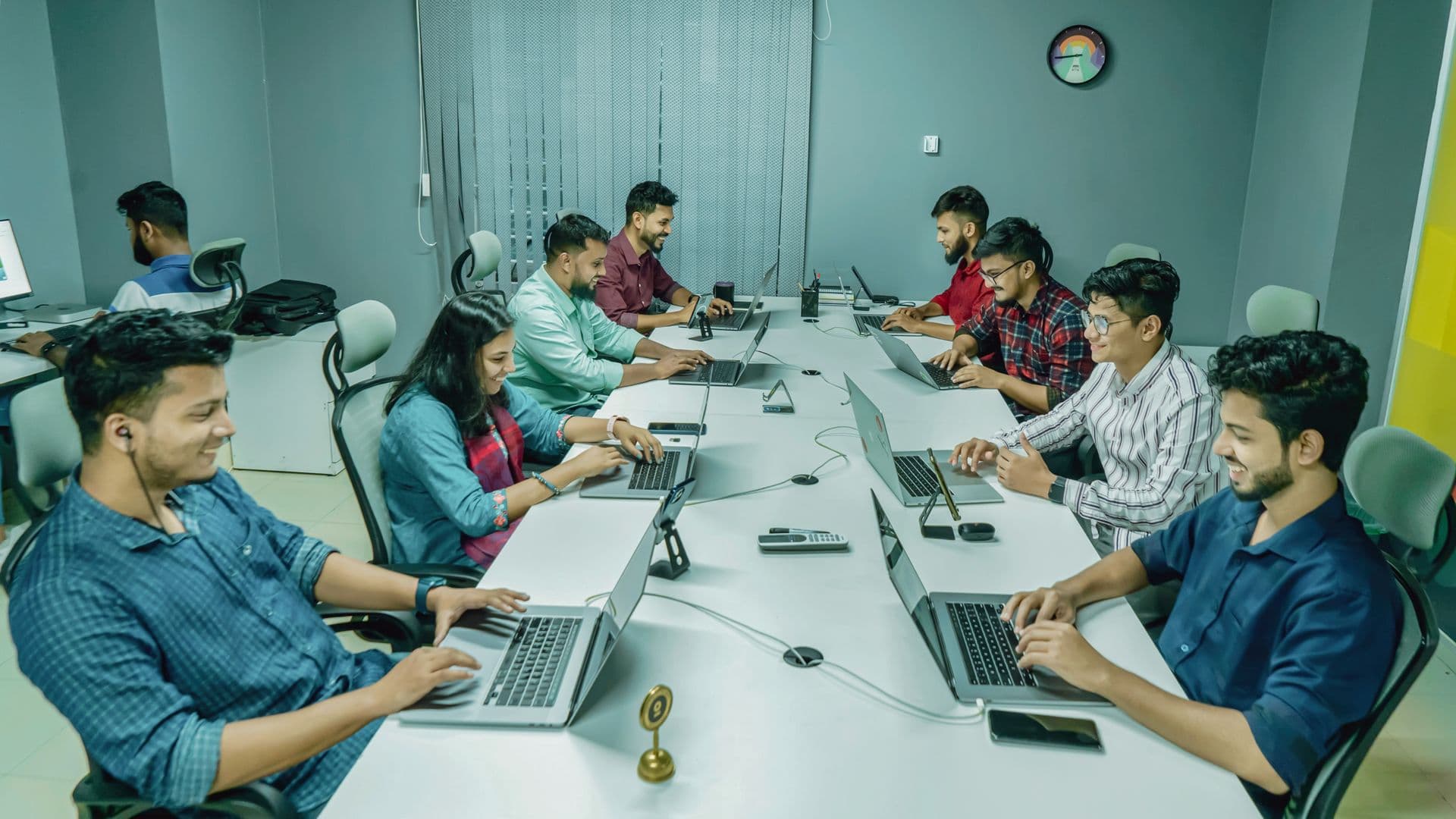 Team of young professionals working on laptops along a long shared office desk