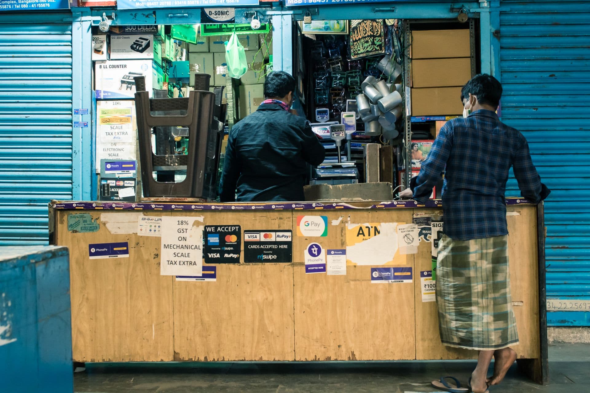 Two men at a shop counter covered in card and digital payment stickers