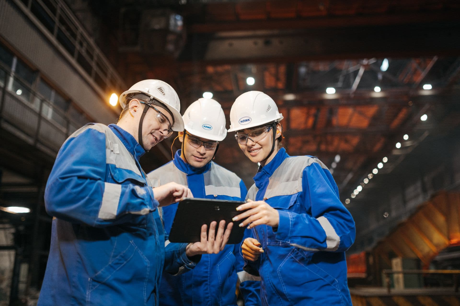 Three engineers in hard hats reviewing a tablet together on a factory floor