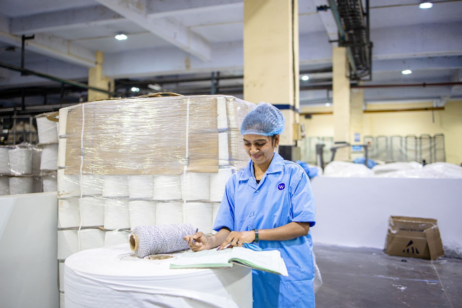 Textile factory worker in a blue uniform and hairnet recording production details by hand