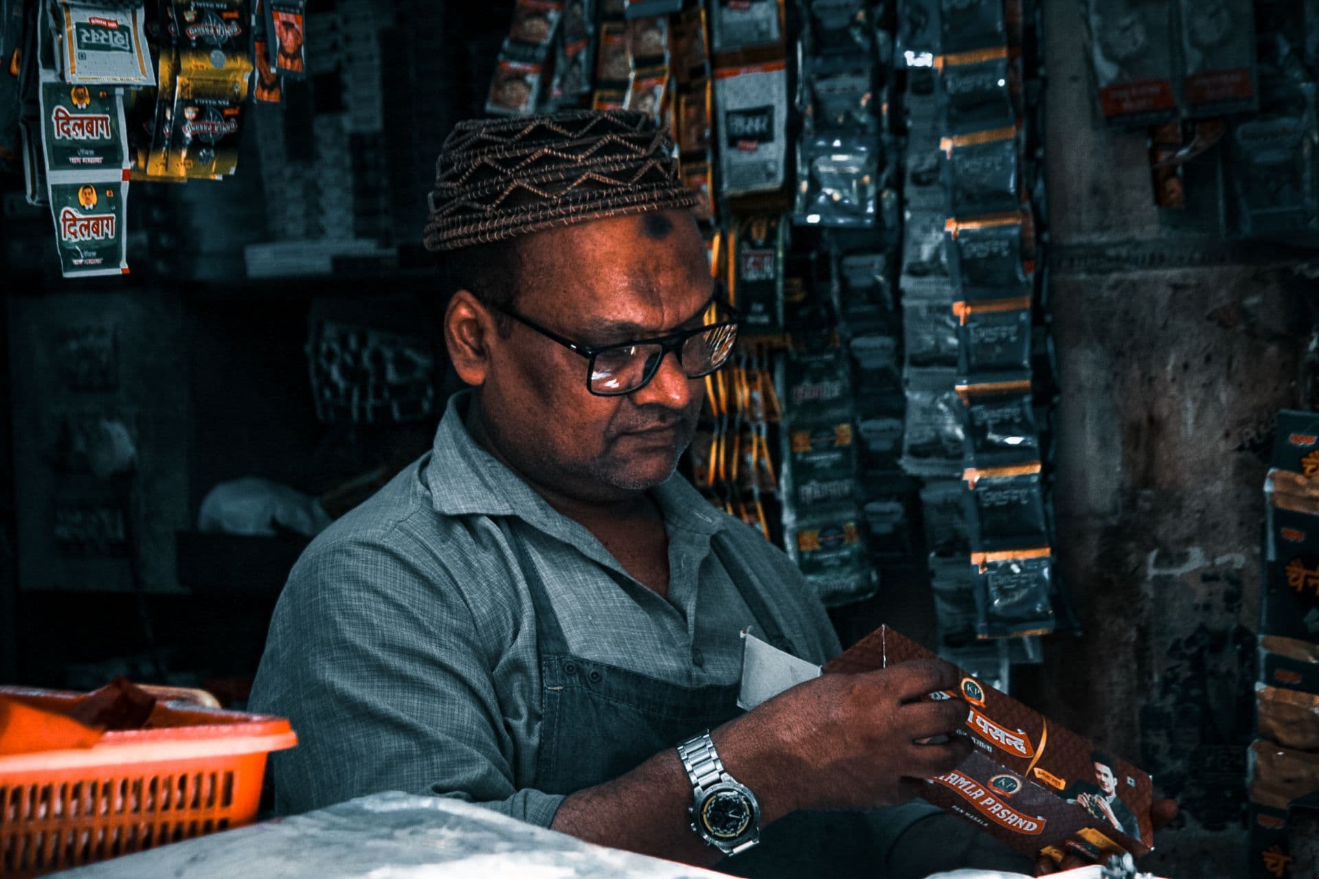 Shopkeeper in glasses and a knitted cap opens a product packet in his store