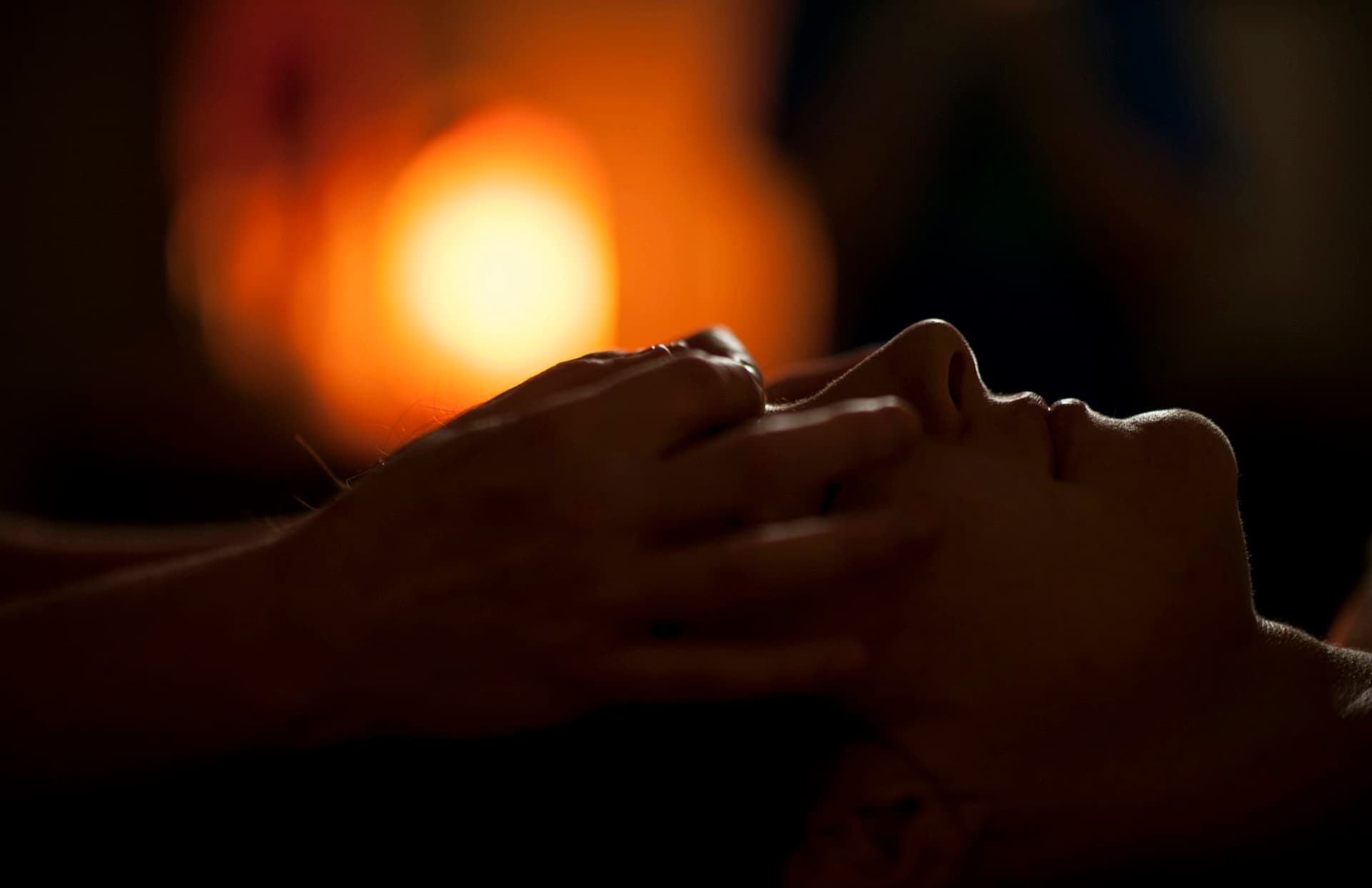 Hands giving a relaxing face massage in a dimly lit spa room with warm glowing light