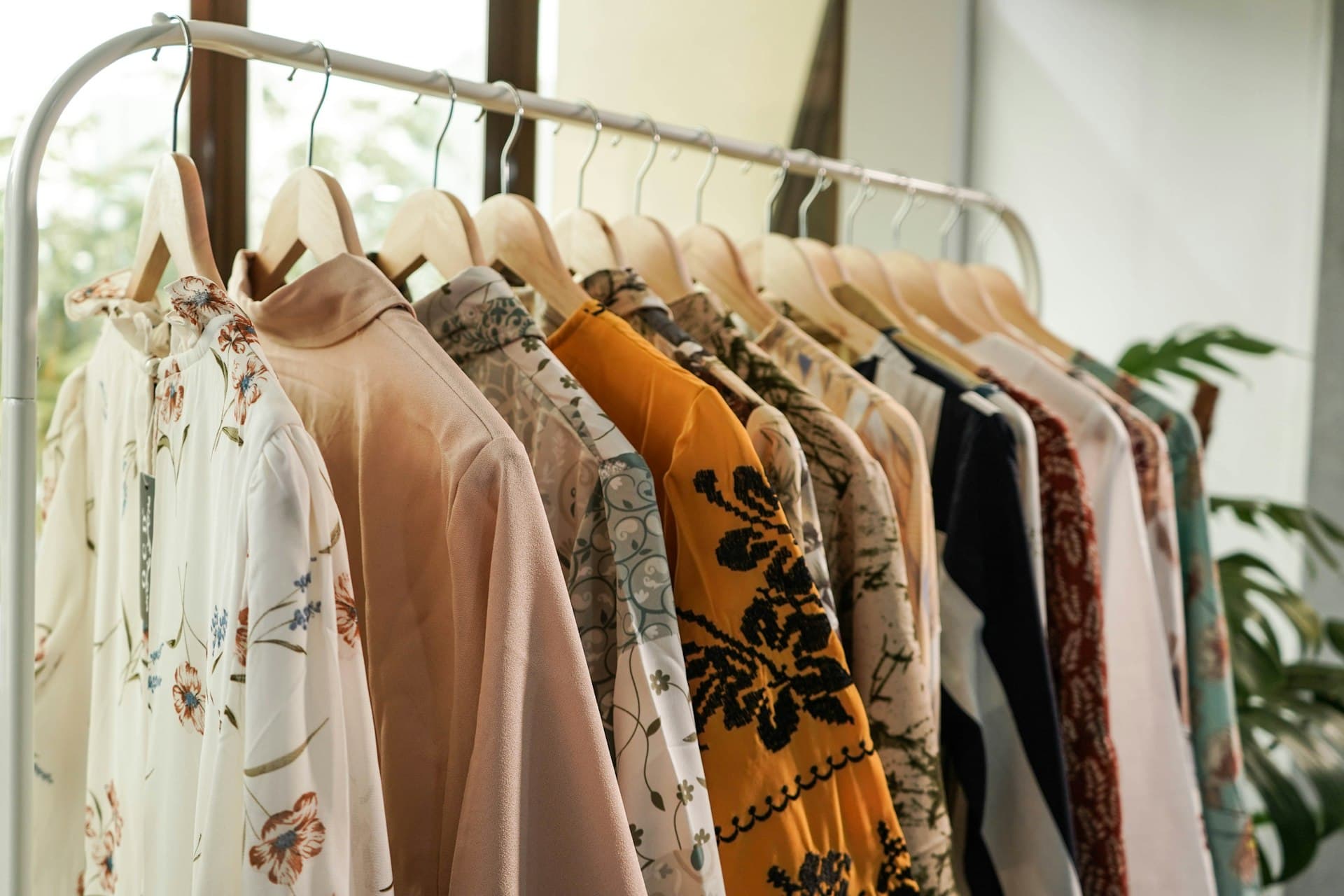 Patterned and floral blouses hanging on wooden hangers on a clothing rail in a boutique
