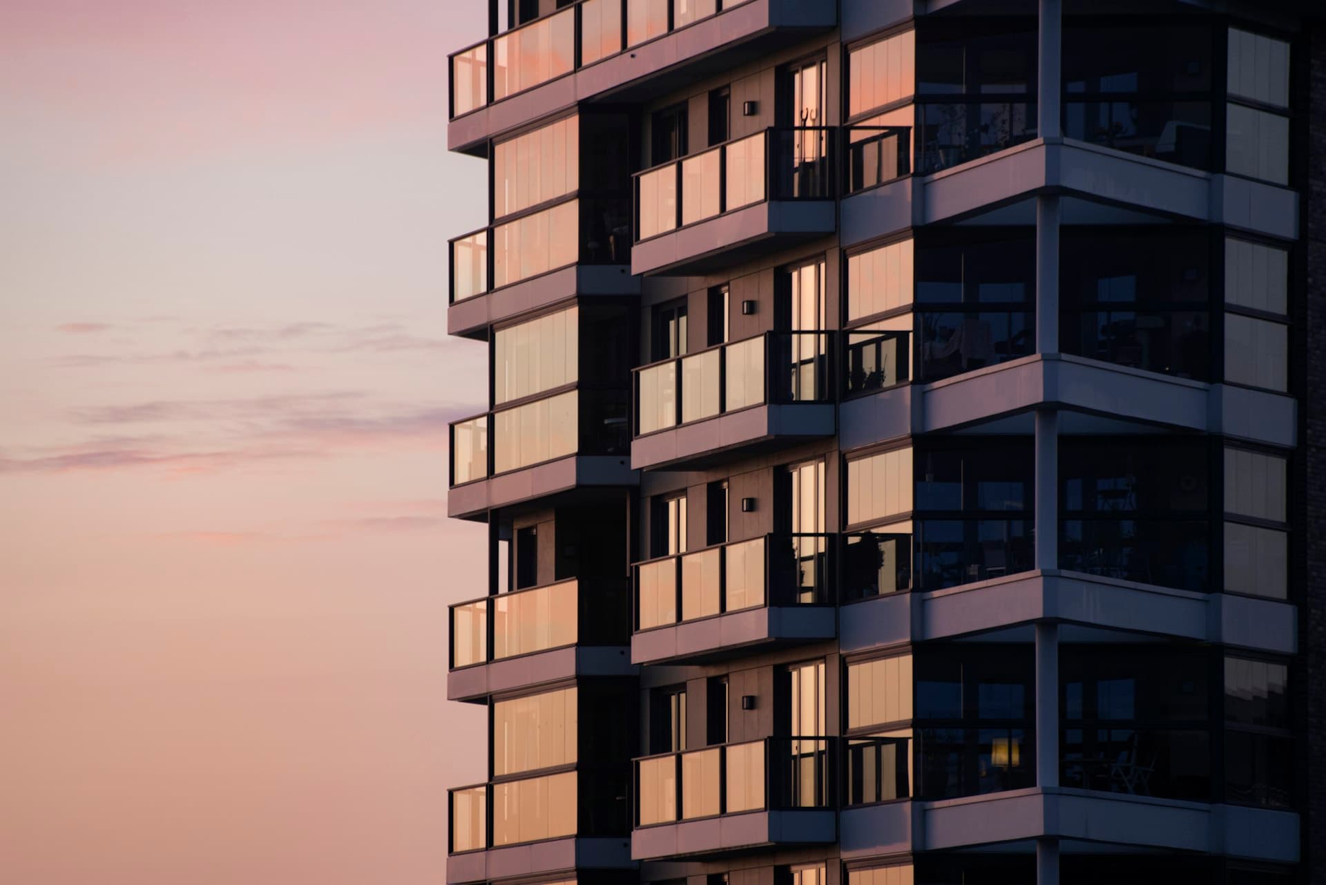 Modern apartment tower with glass-fronted balconies against a soft pink dusk sky