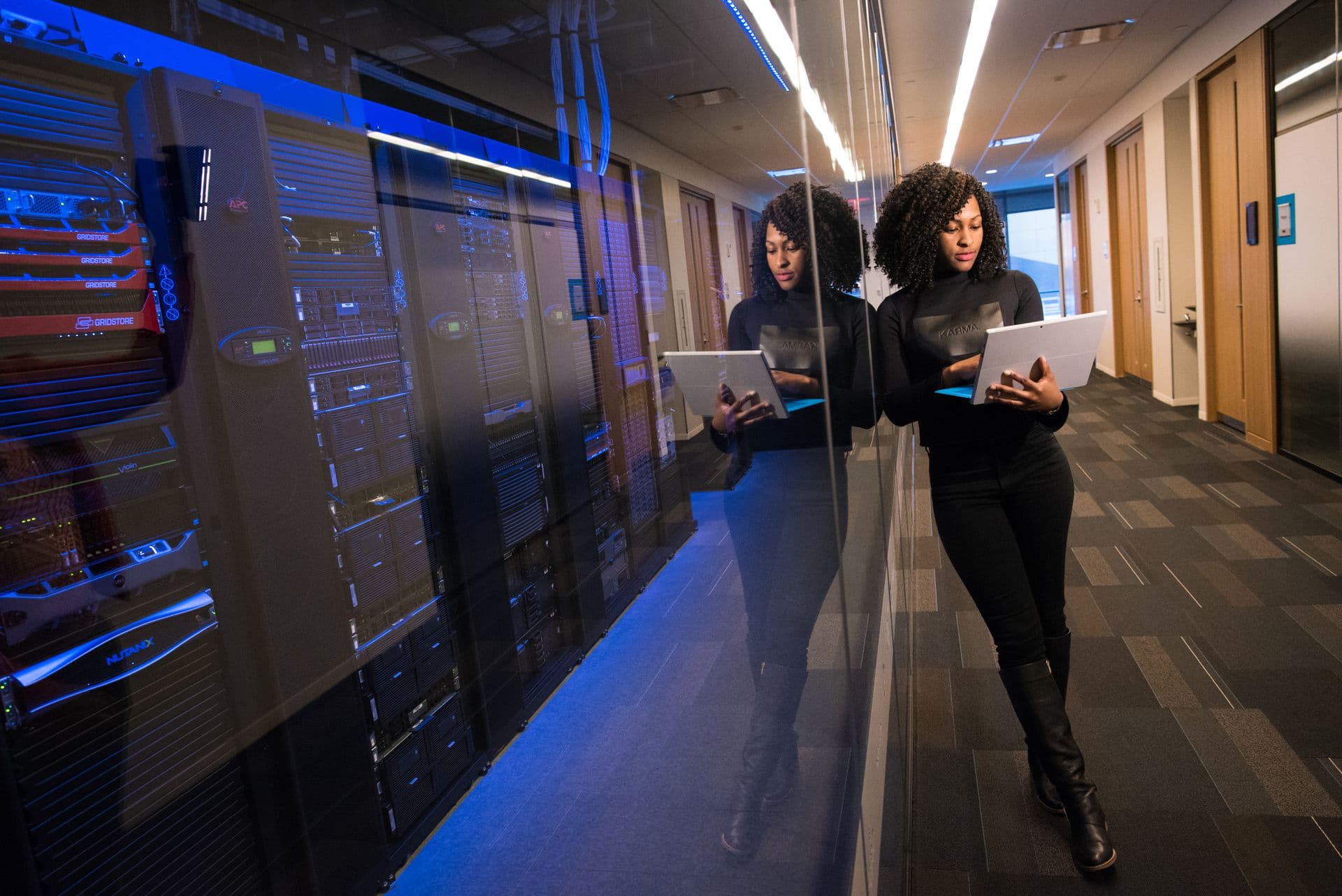 Woman holding a laptop beside illuminated server racks in a data centre corridor