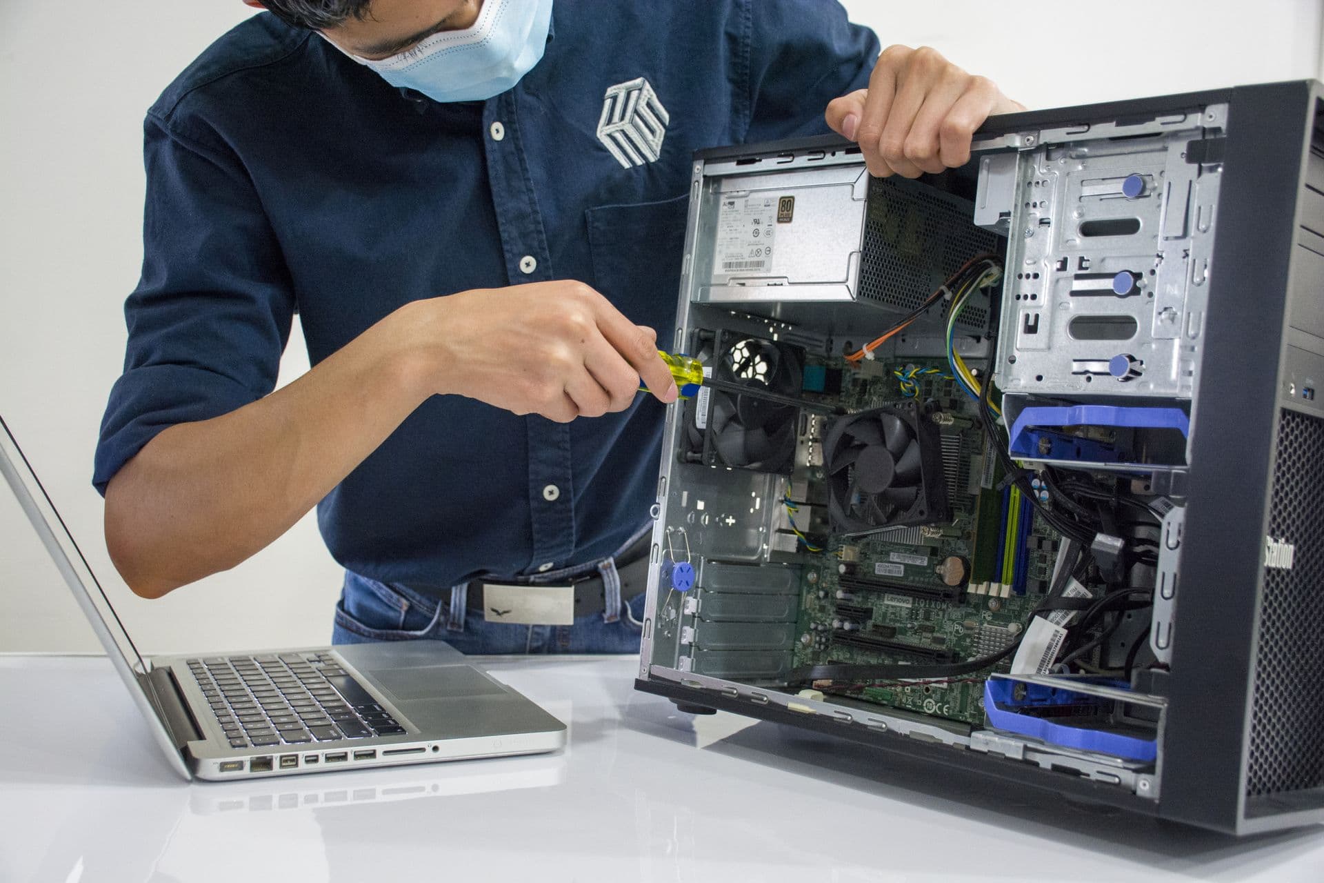 Technician in a face mask repairing an open desktop computer with a screwdriver