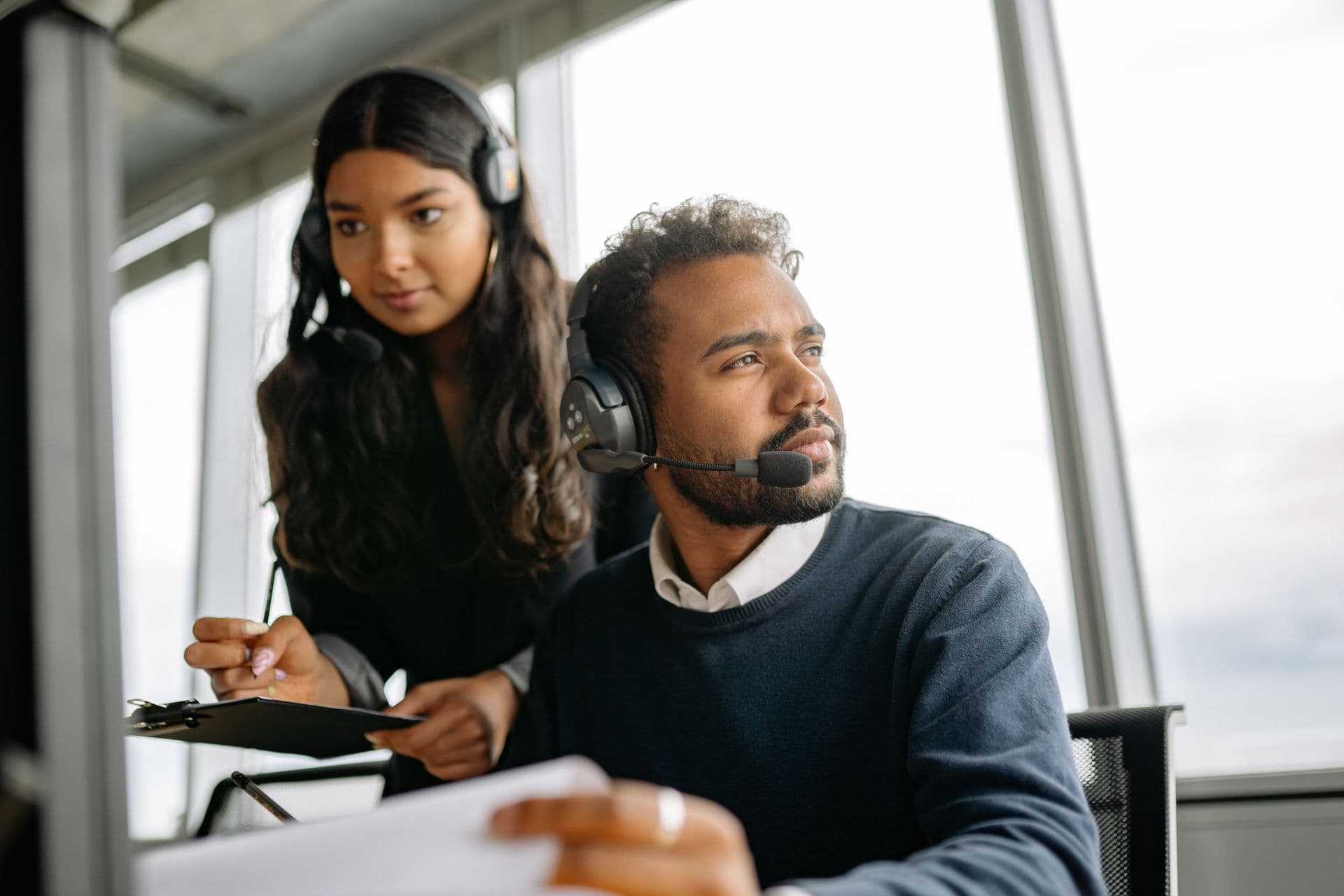 Man and woman wearing headsets working together at a desk by a window