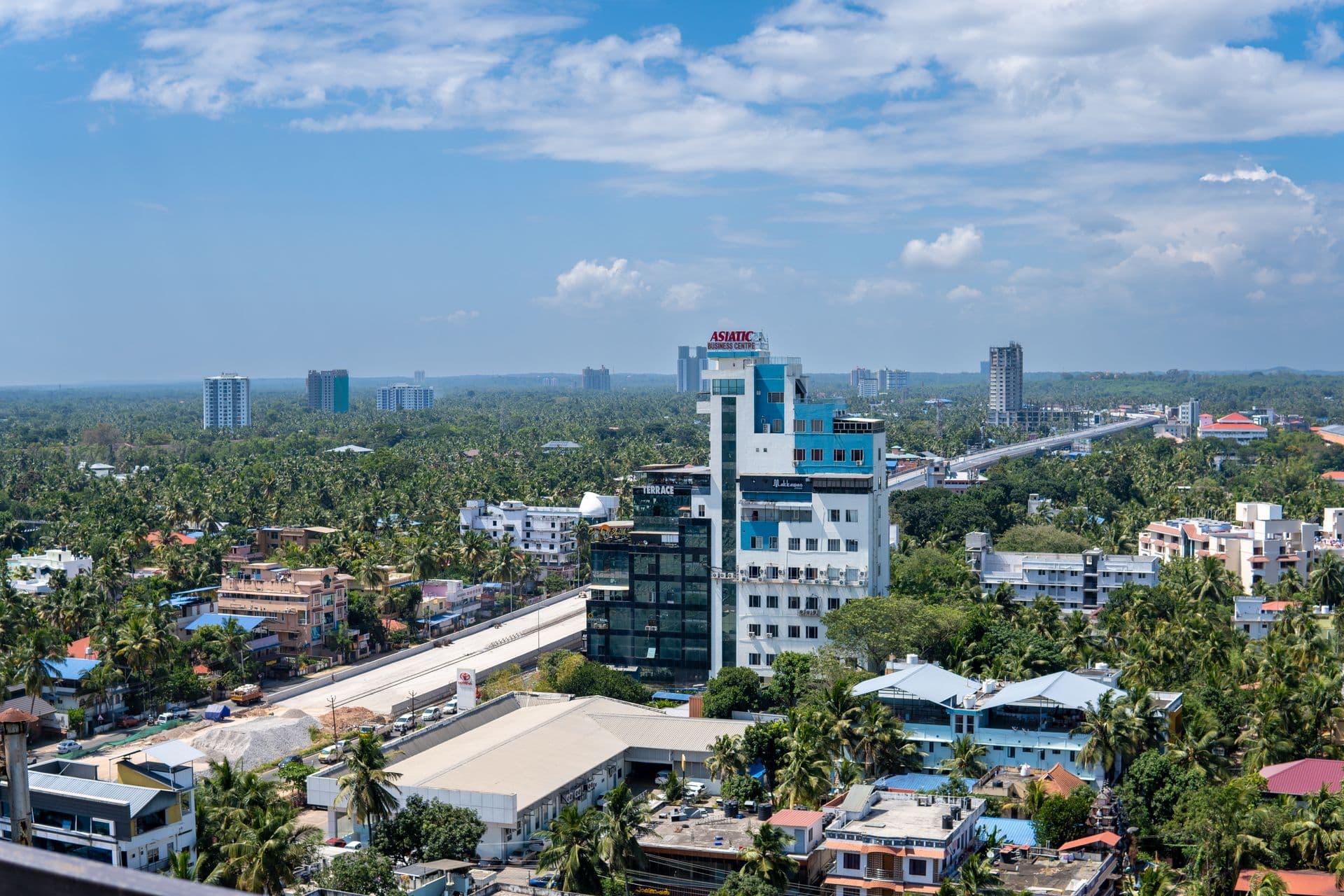 Aerial view of Thiruvananthapuram with a glass office tower among coconut palms
