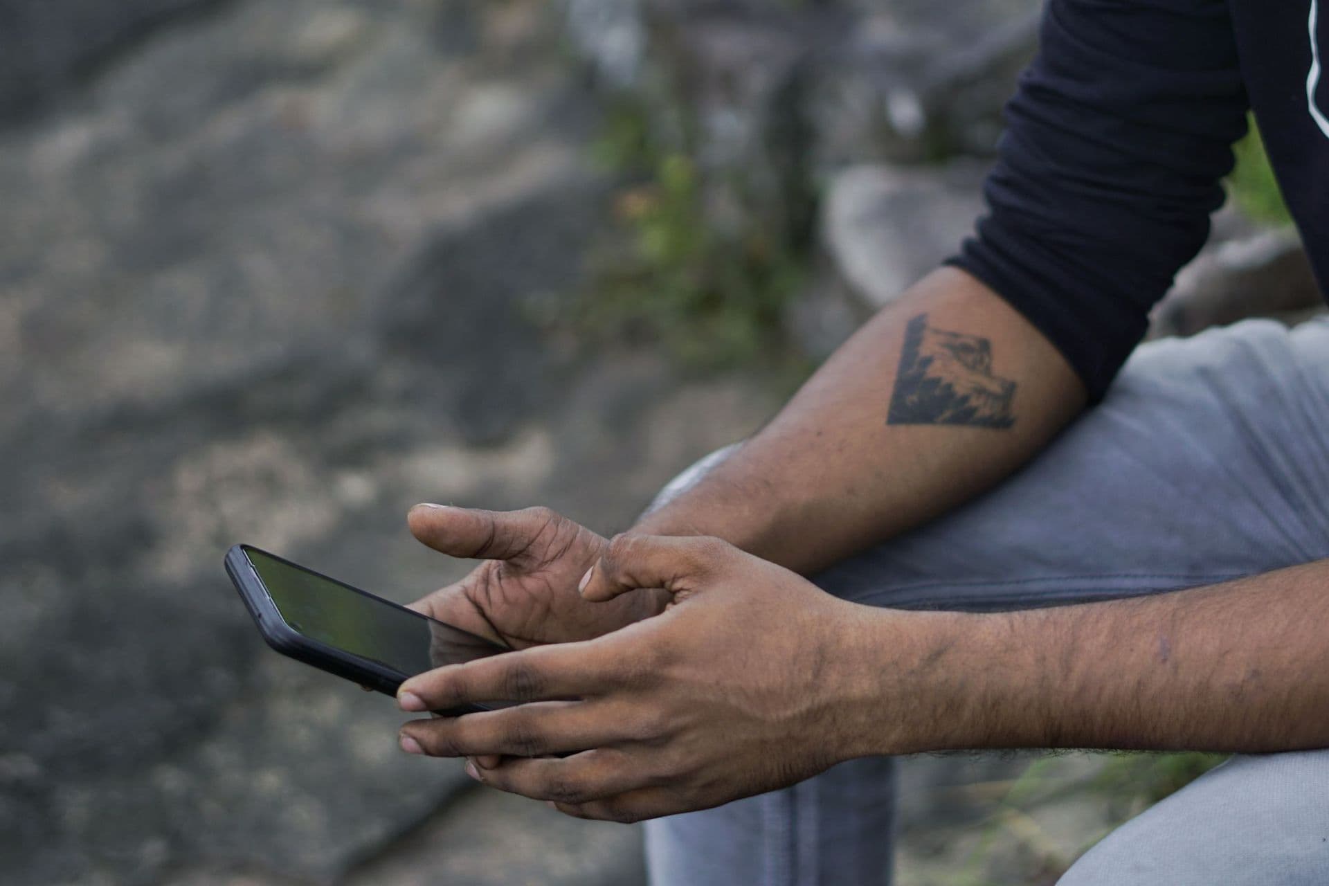 Close-up of a man's hands holding a smartphone while sitting outdoors