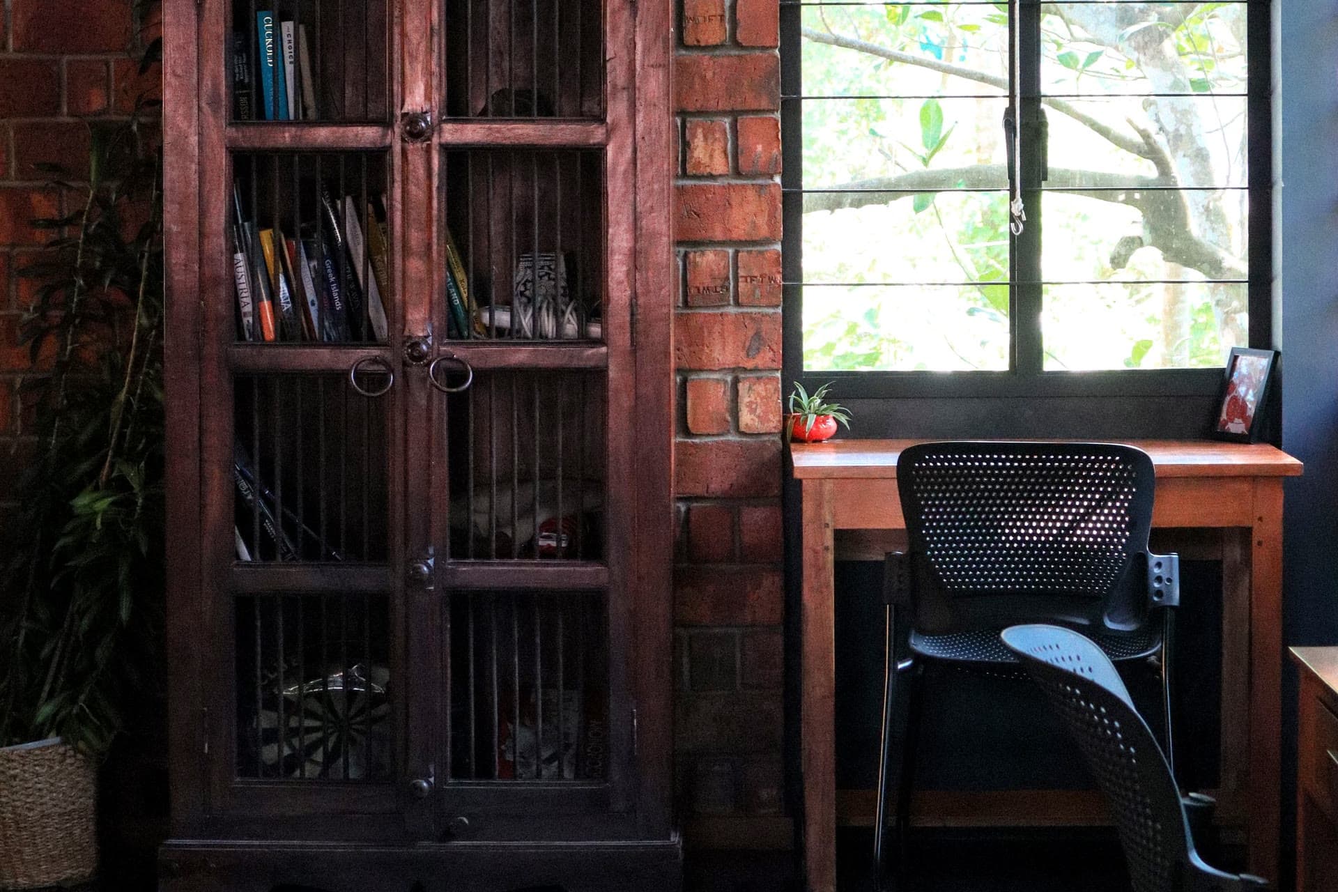 Office corner with a wooden bookcase, exposed brick wall and desk by a sunlit window