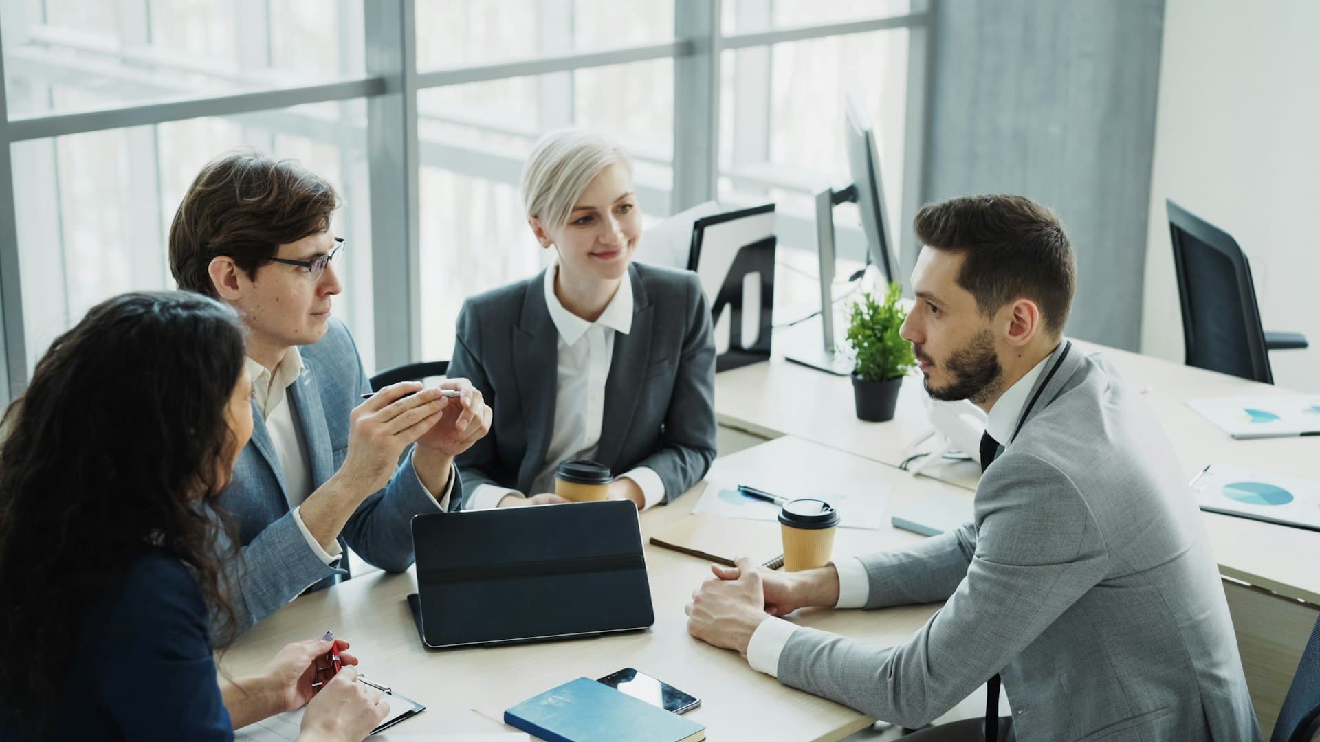 Four colleagues in business attire discussing ideas around a table in a bright meeting room