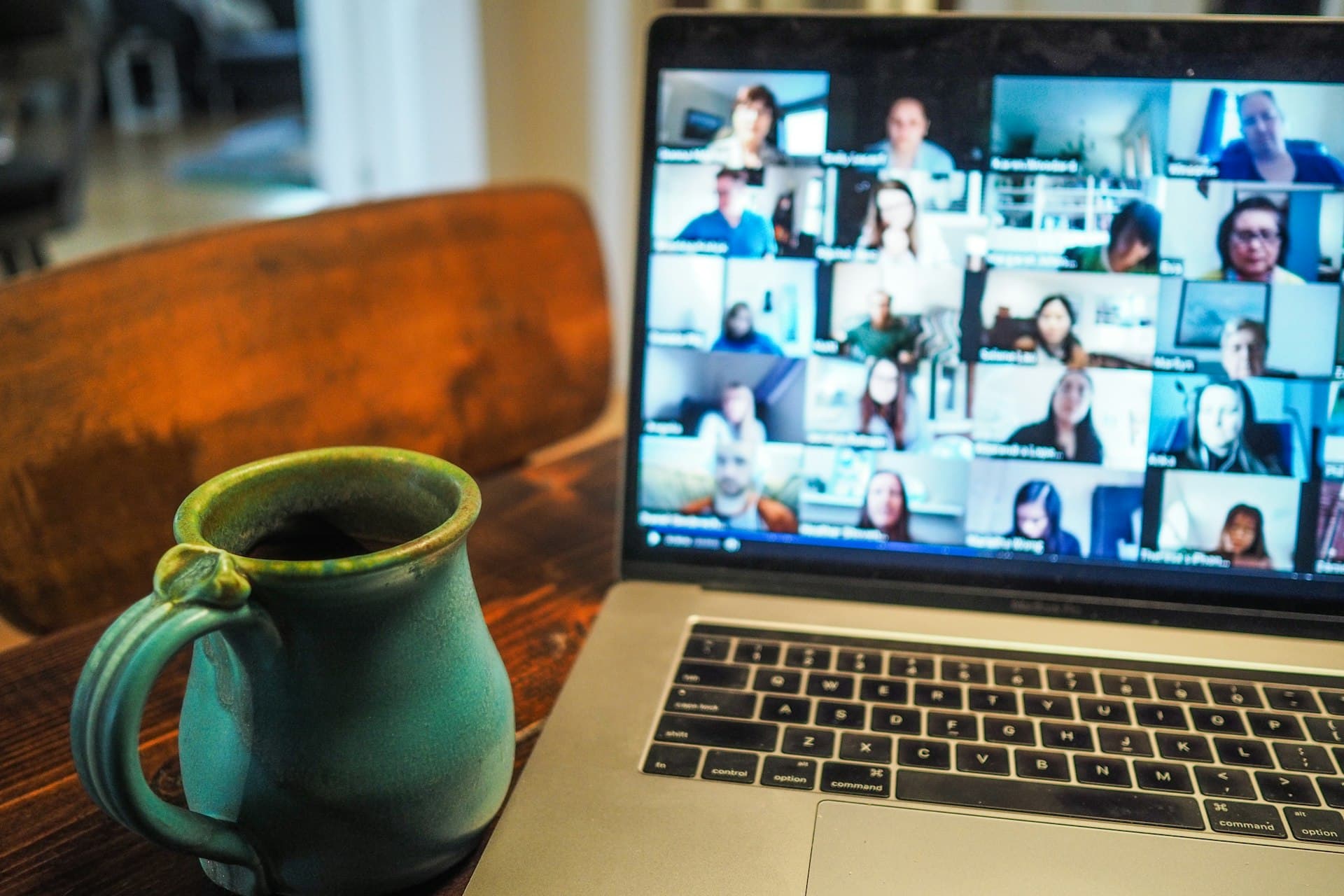 Laptop screen showing a video call grid of many participants beside a green ceramic coffee mug