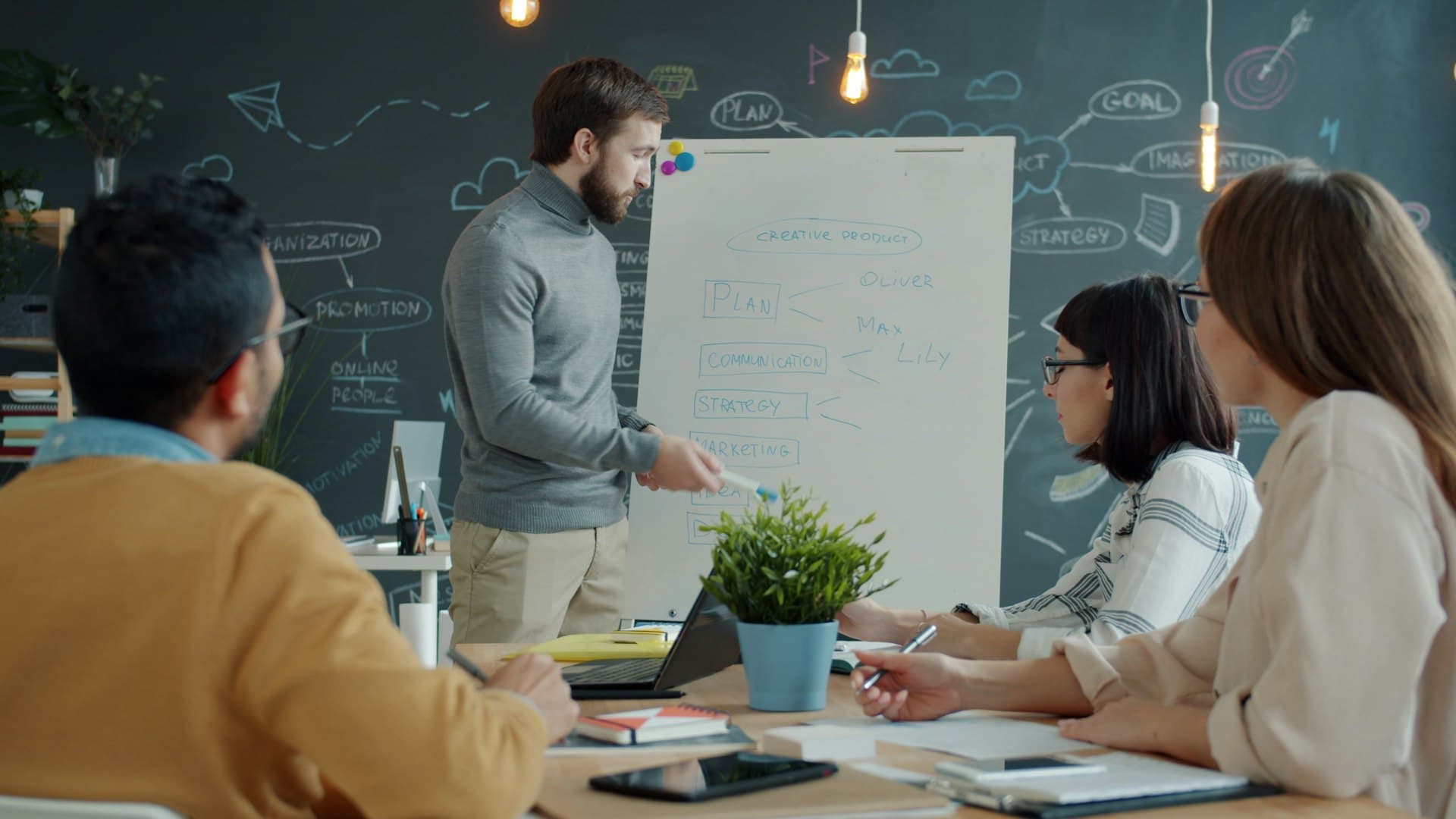Man presenting plans on a whiteboard to three colleagues seated at a table