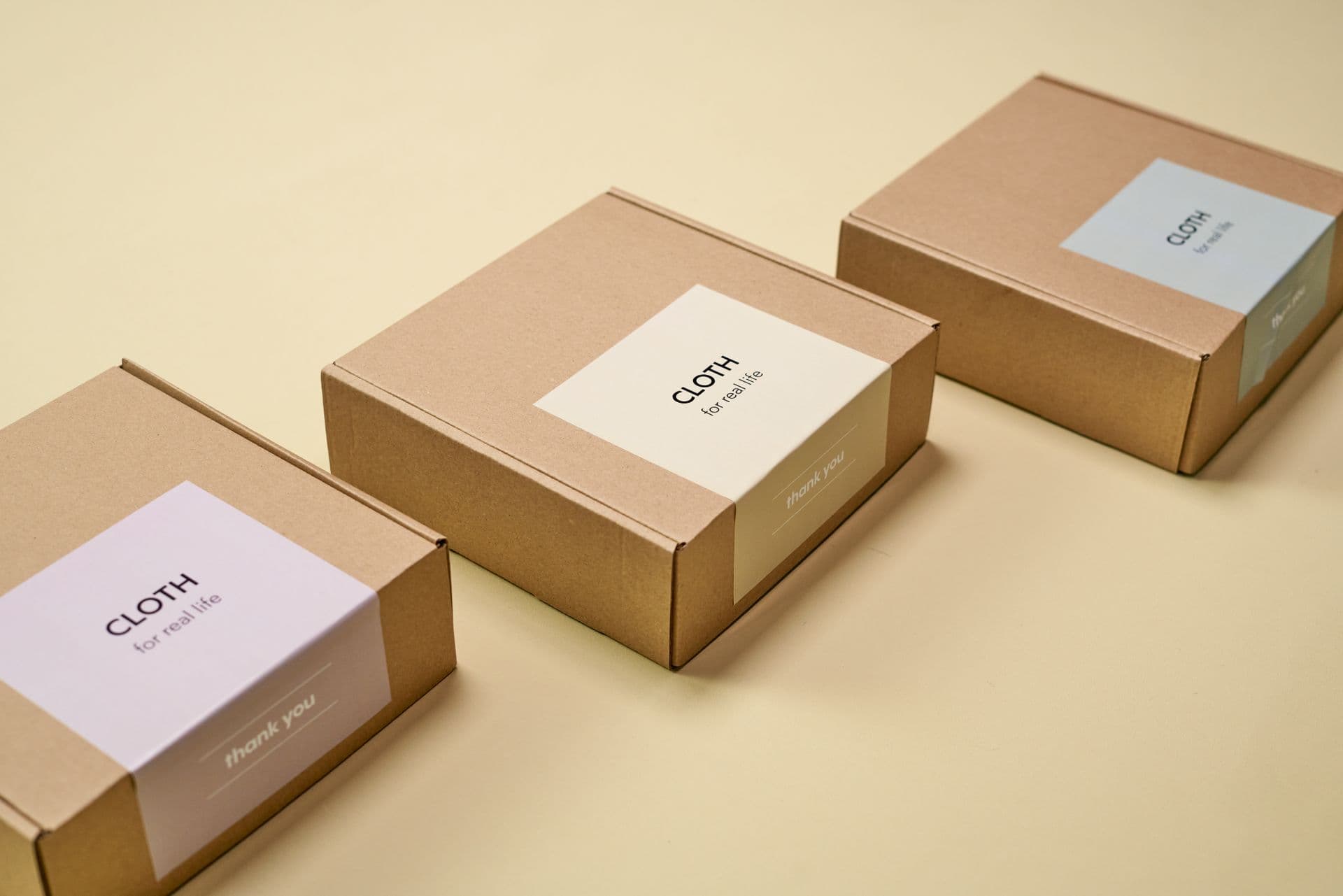 Three kraft mailer boxes with pastel CLOTH labels on a yellow surface