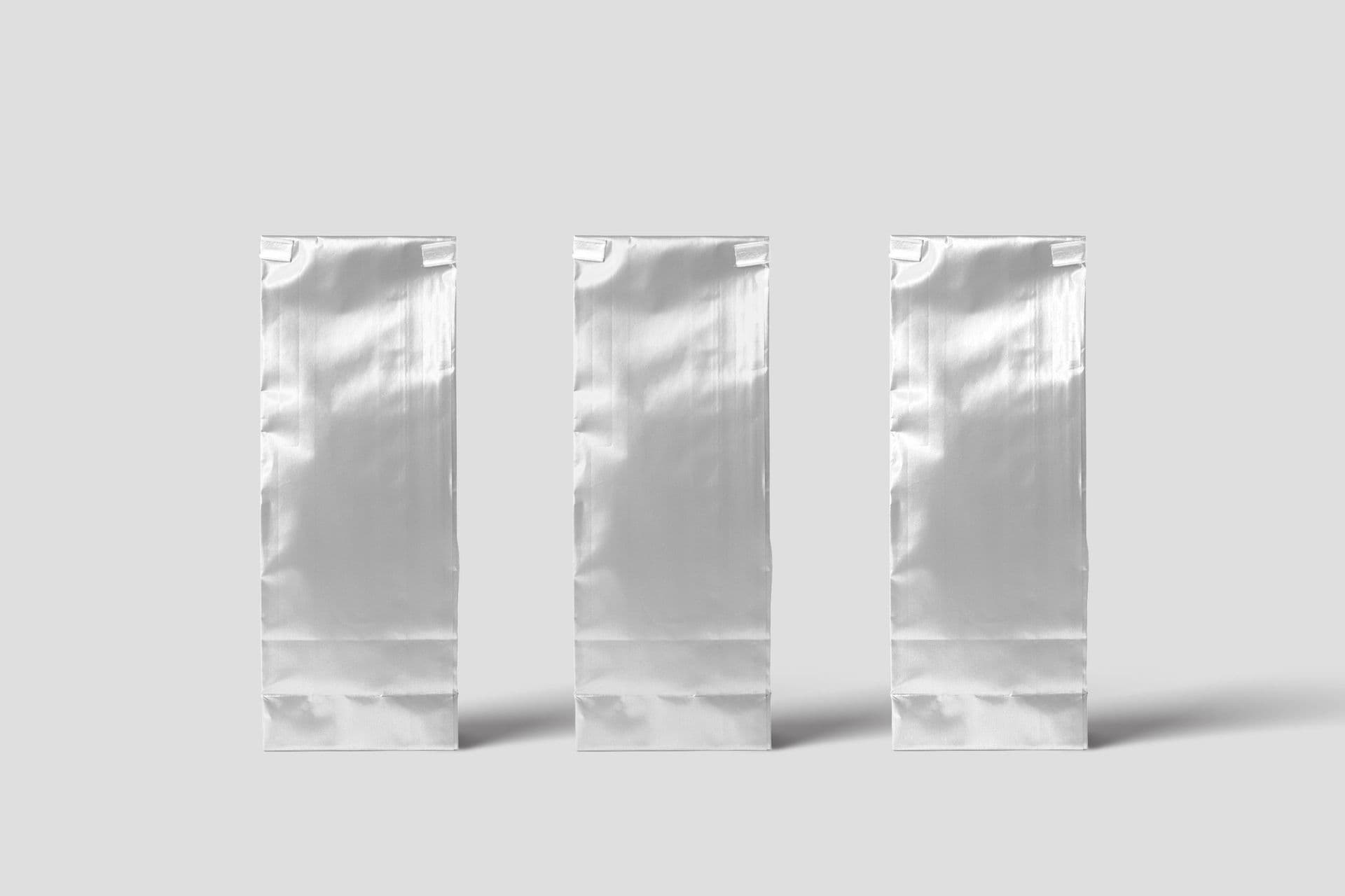 Three blank silver foil pouches standing in a row on a light grey background