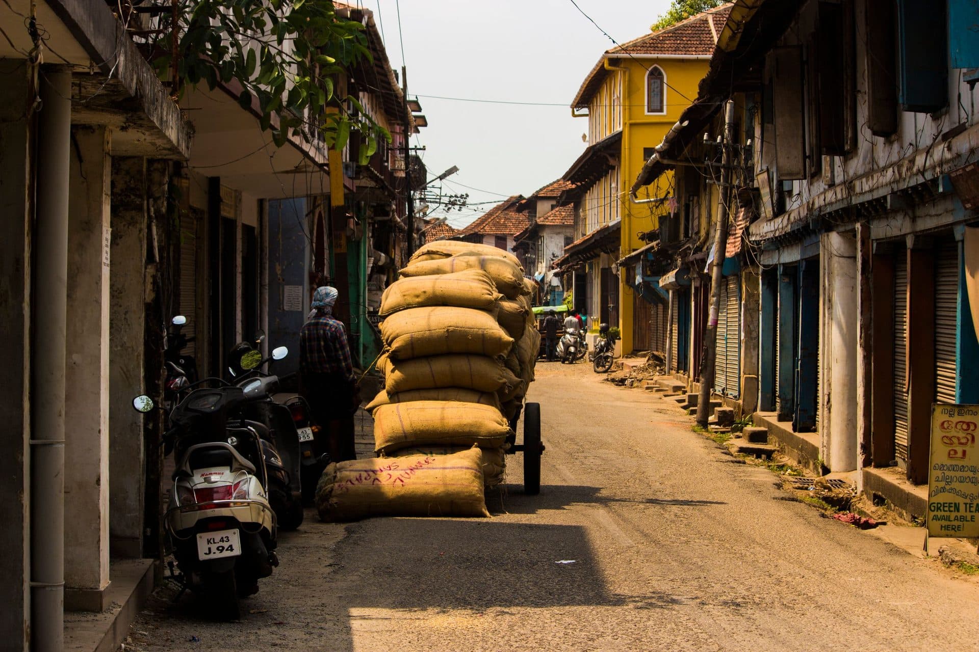 Burlap sacks piled on a handcart in a narrow street lined with old shuttered buildings