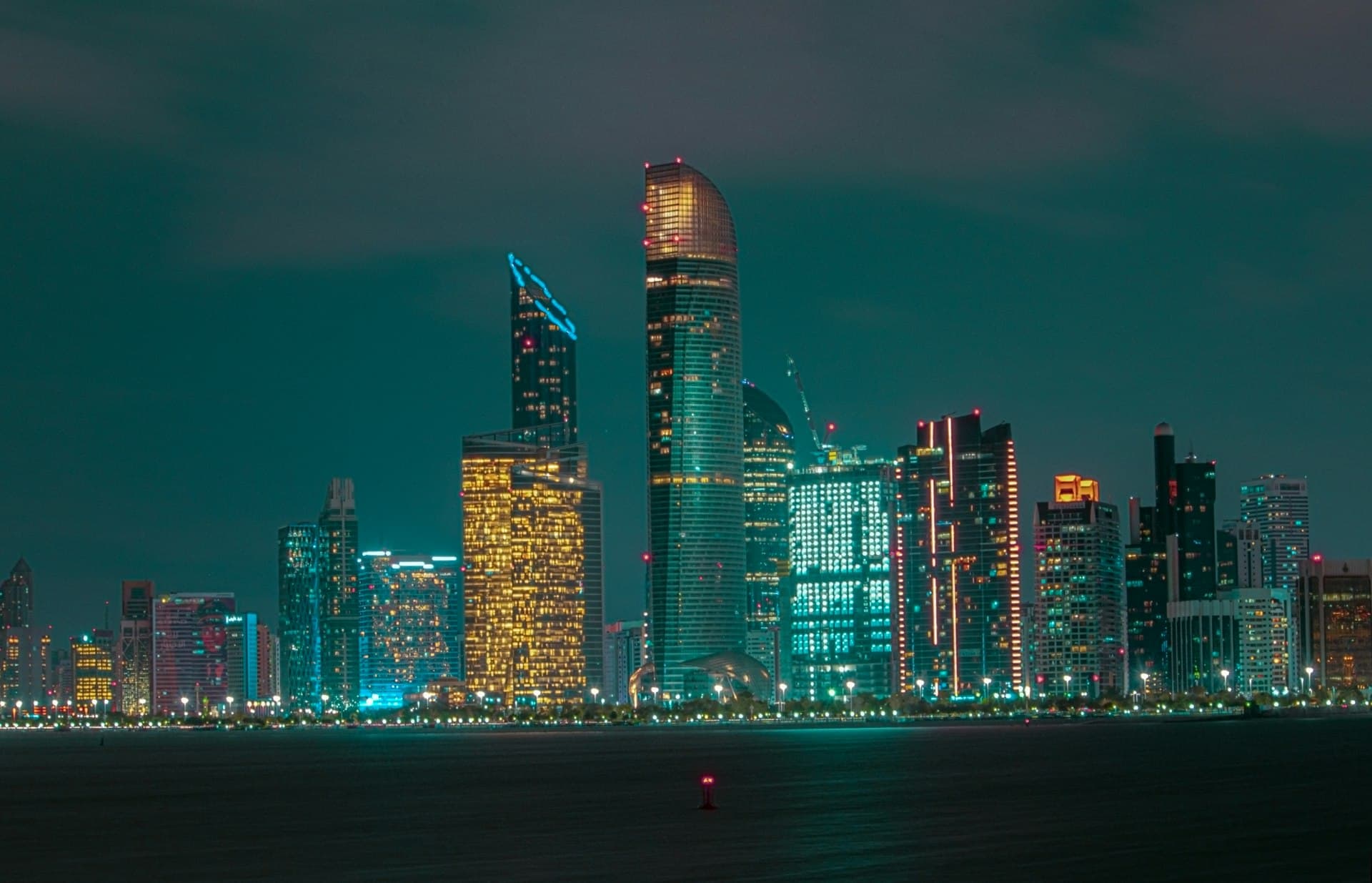 Abu Dhabi skyline lit up at night, seen across the water from the Corniche breakwater