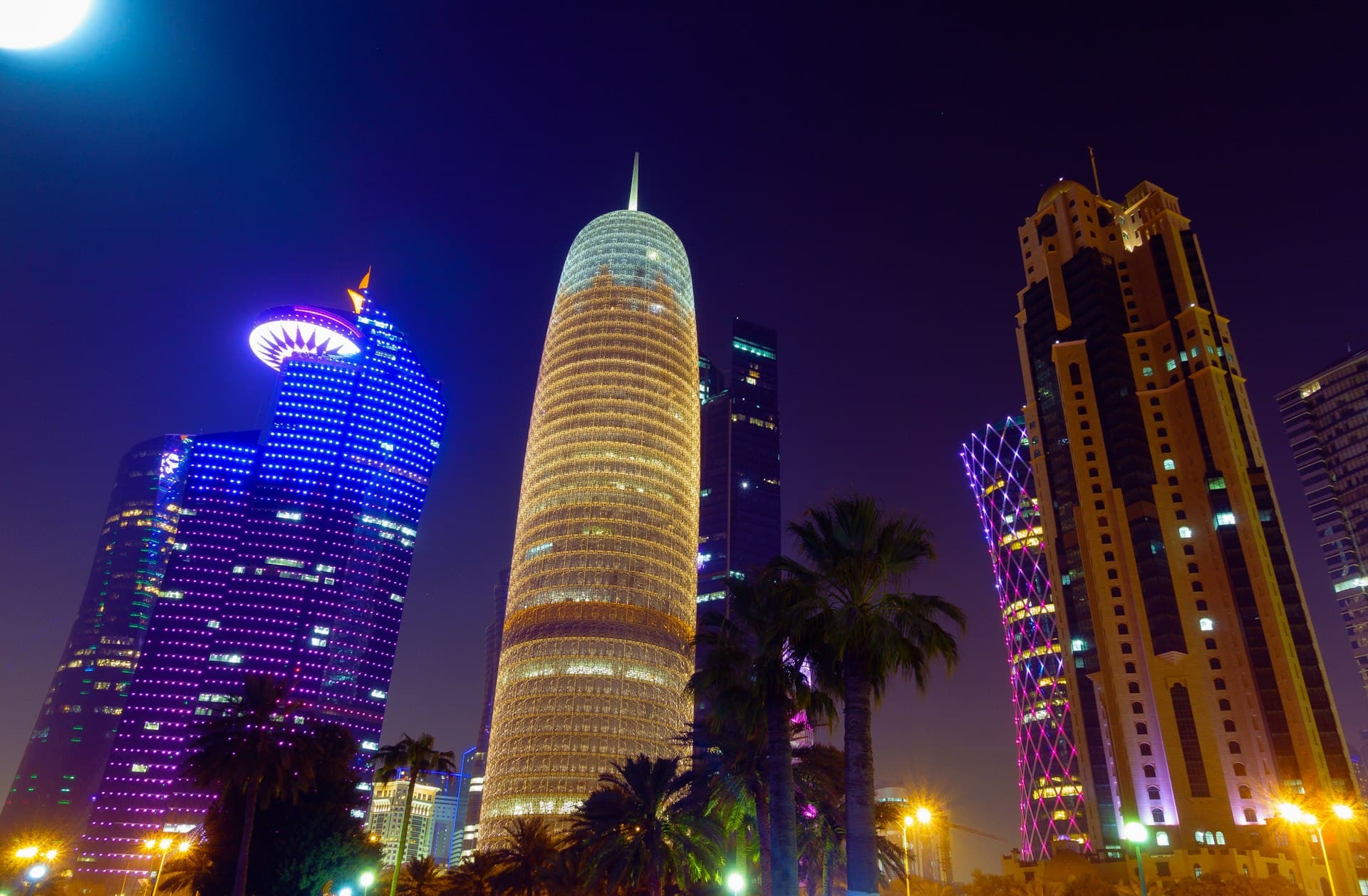 Illuminated skyscrapers and palm trees in the West Bay district of Doha, Qatar, at night
