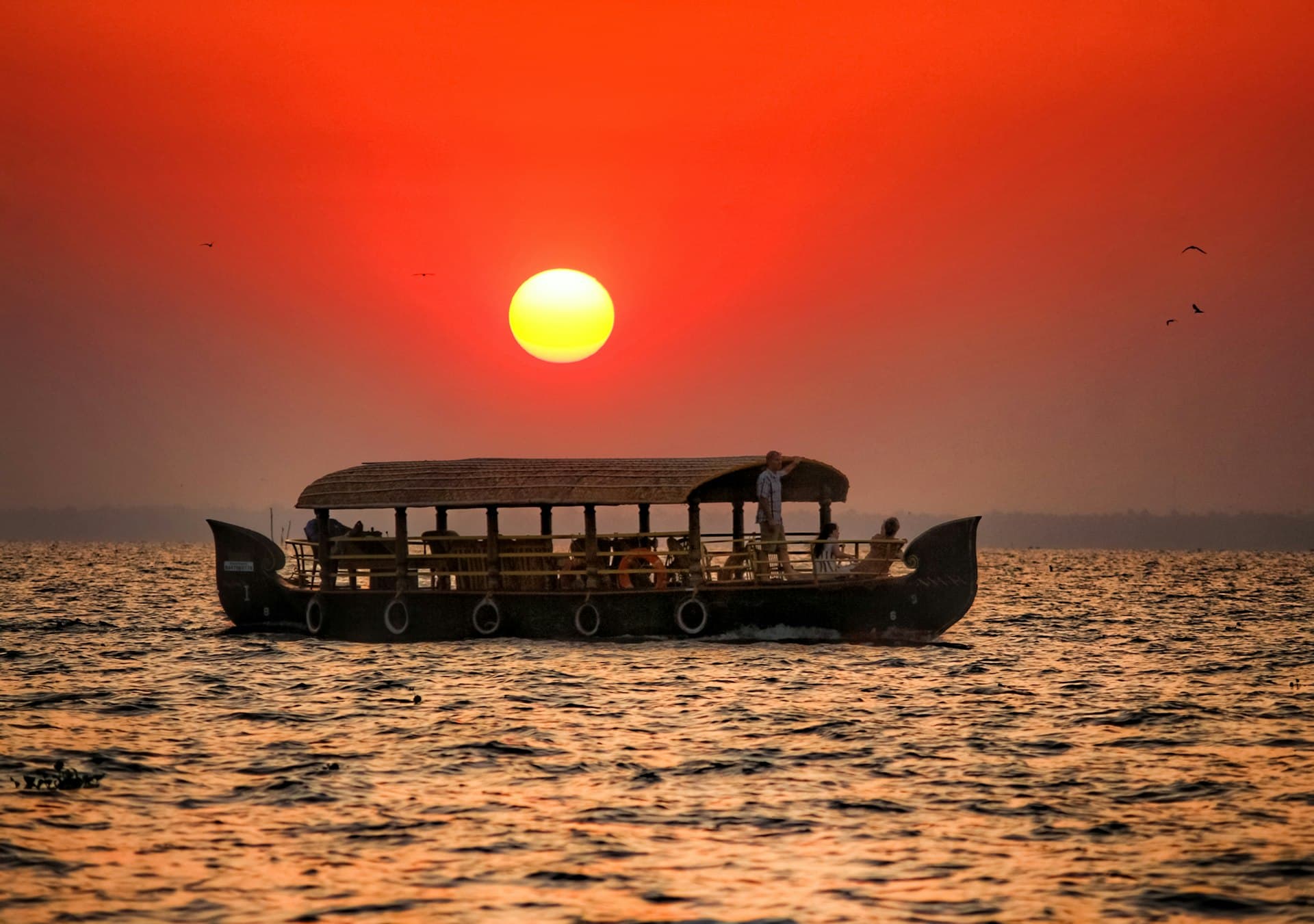 Traditional Kerala houseboat silhouetted against a red sunset on the backwaters at Kumarakom