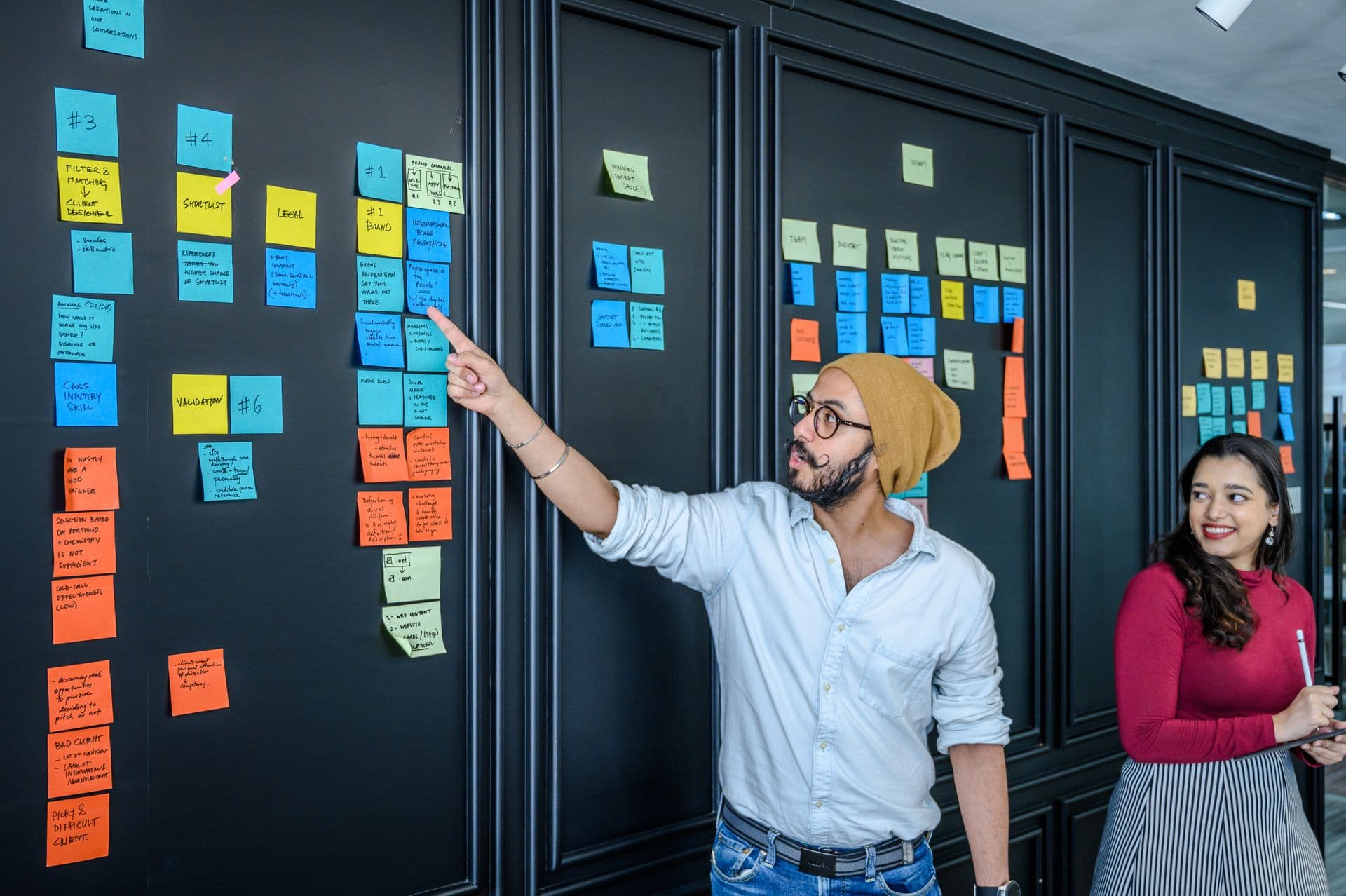 Man pointing at a wall of colourful sticky notes while a colleague looks on