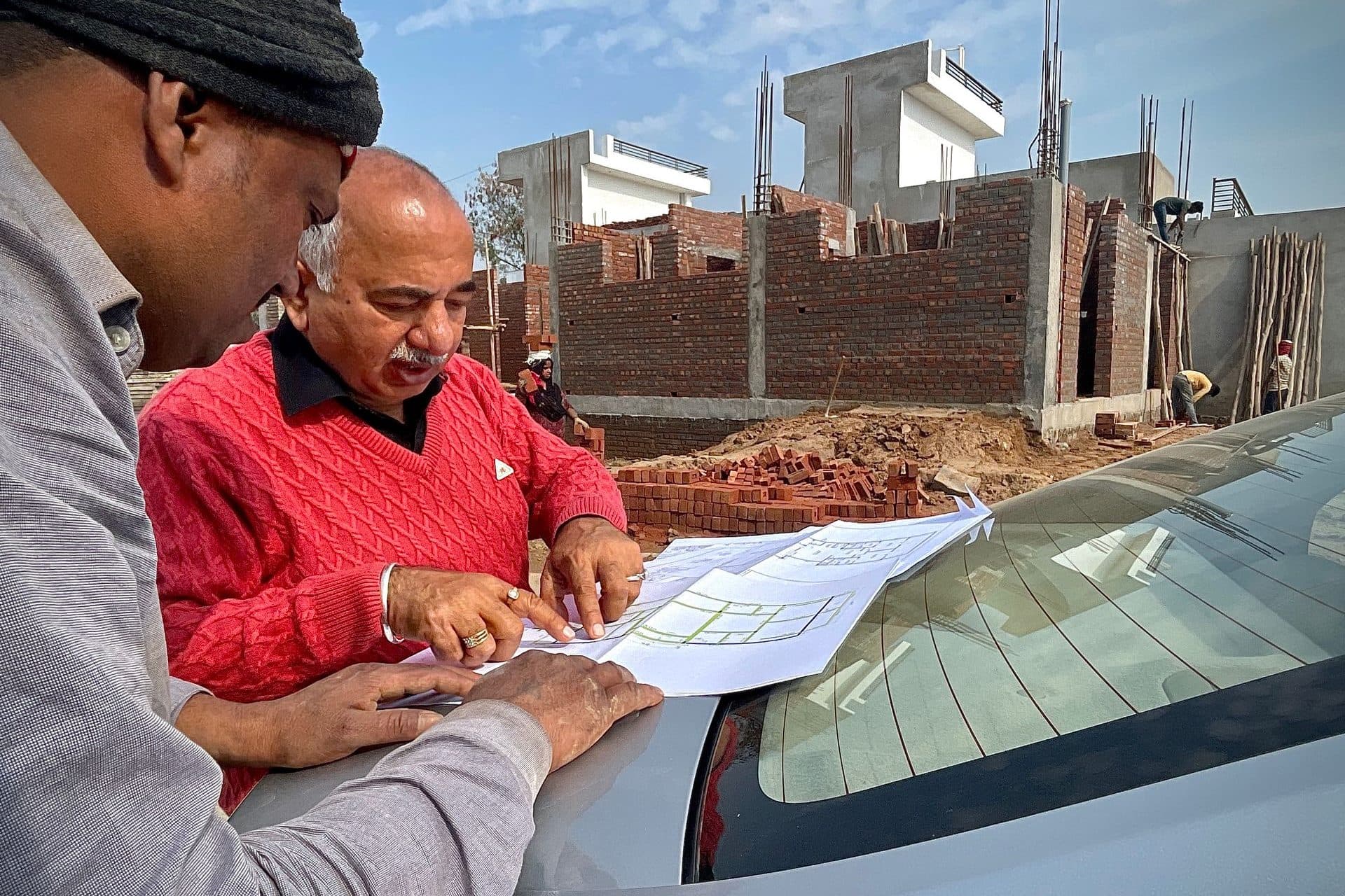 Two men reviewing building plans on a car bonnet at a brick construction site