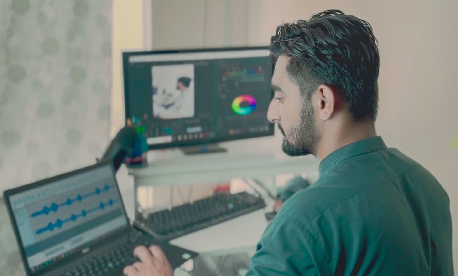 Man editing video and audio at a desk with a monitor and a laptop