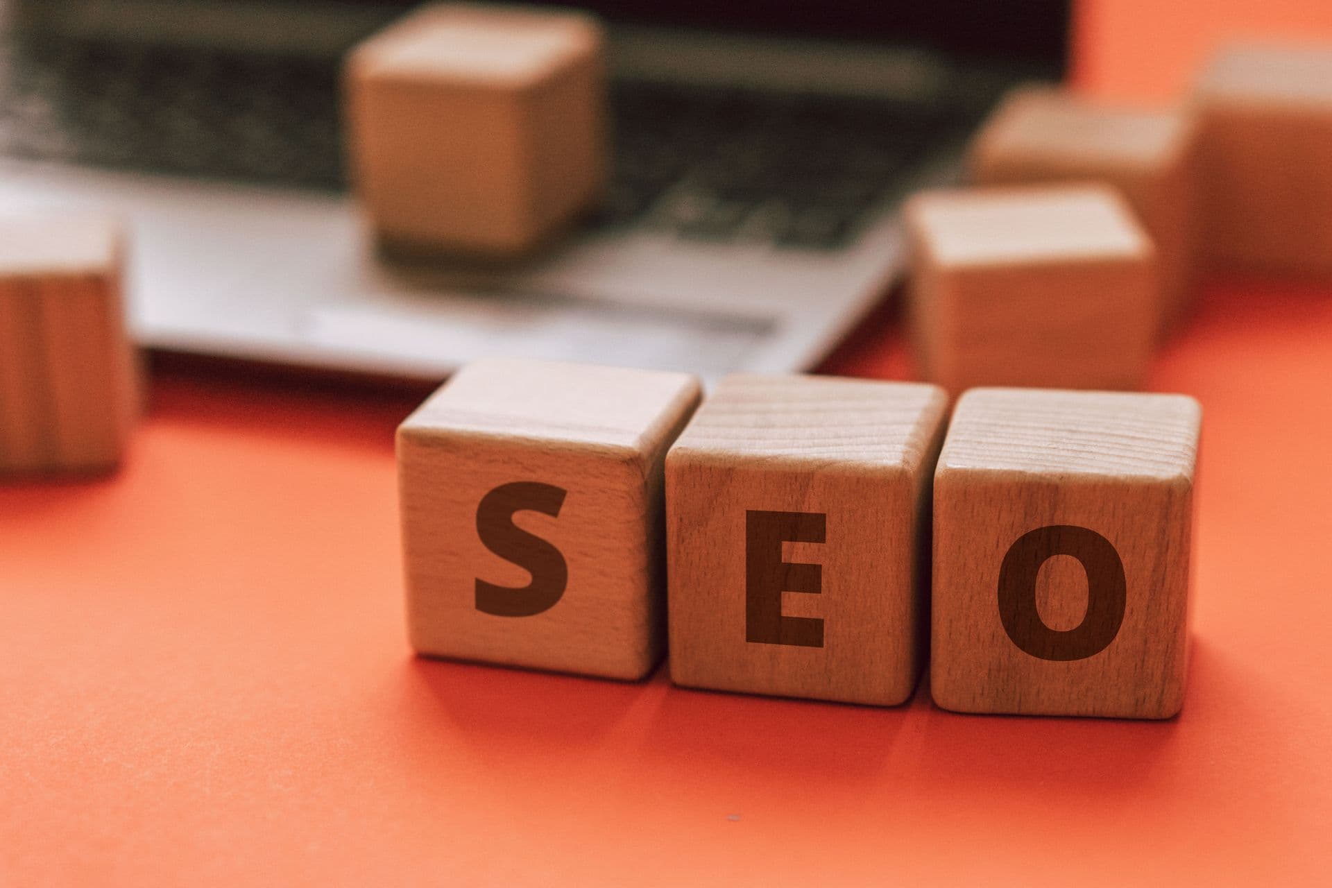 Wooden blocks spelling SEO on an orange desk in front of a laptop