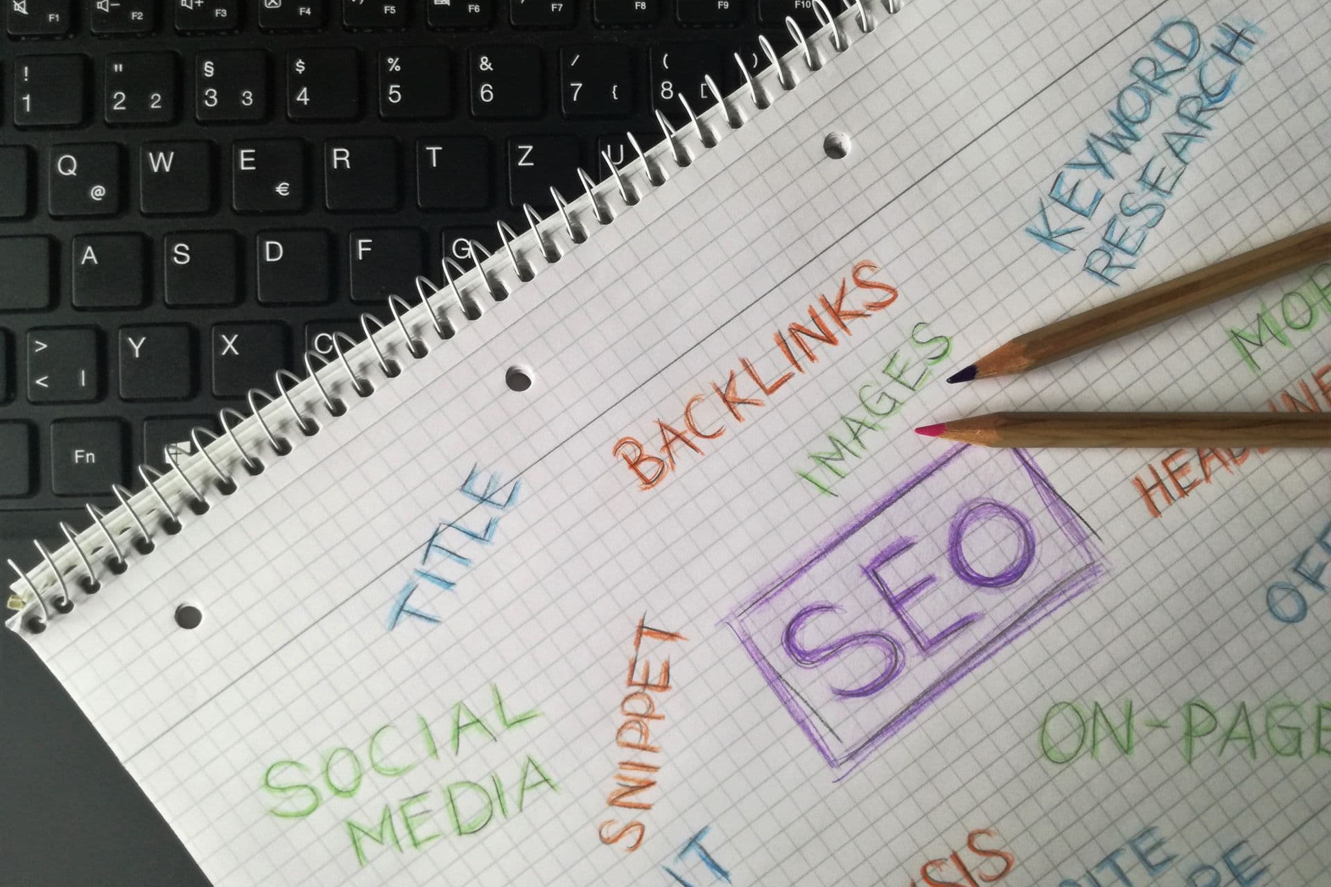 Notebook with handwritten SEO terms like backlinks, keyword research and snippet beside a keyboard