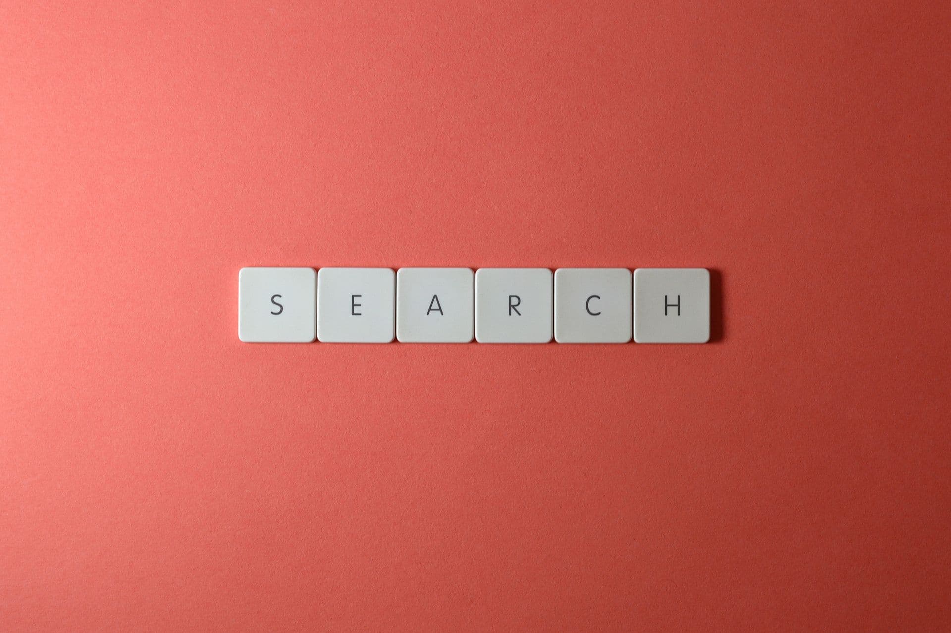 White keyboard keys spelling the word search on a coral red background