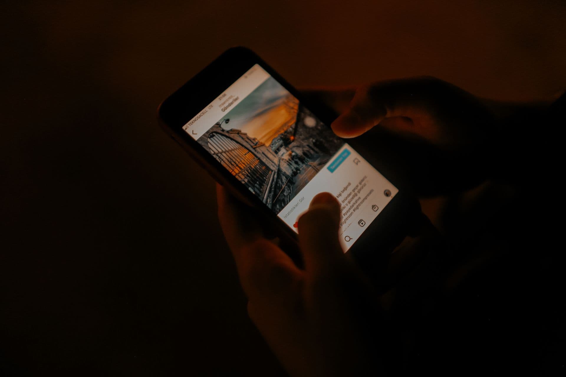 Hands scrolling a social media feed on a smartphone in a dark room