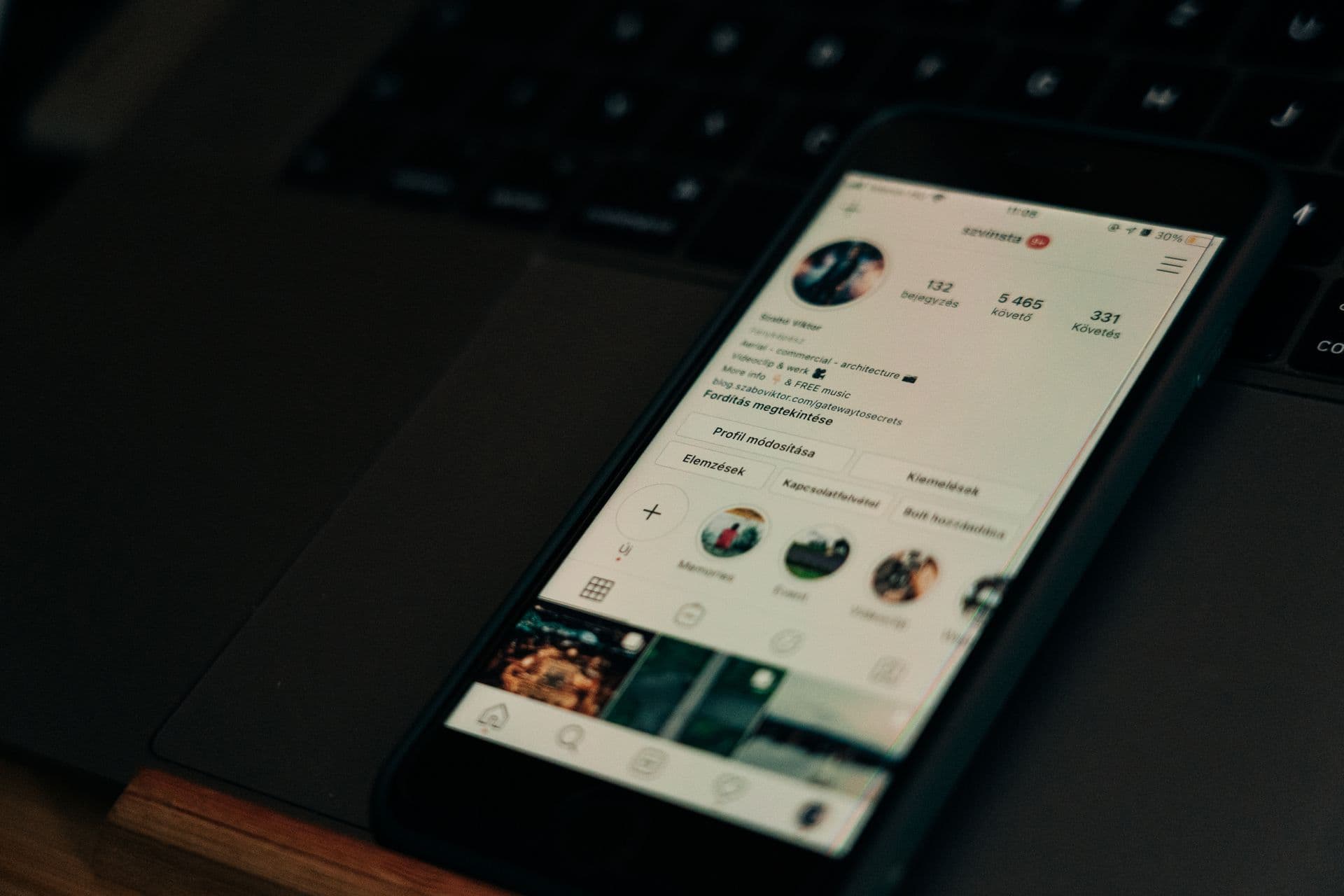 Smartphone showing a social media profile page, resting on a laptop in low light