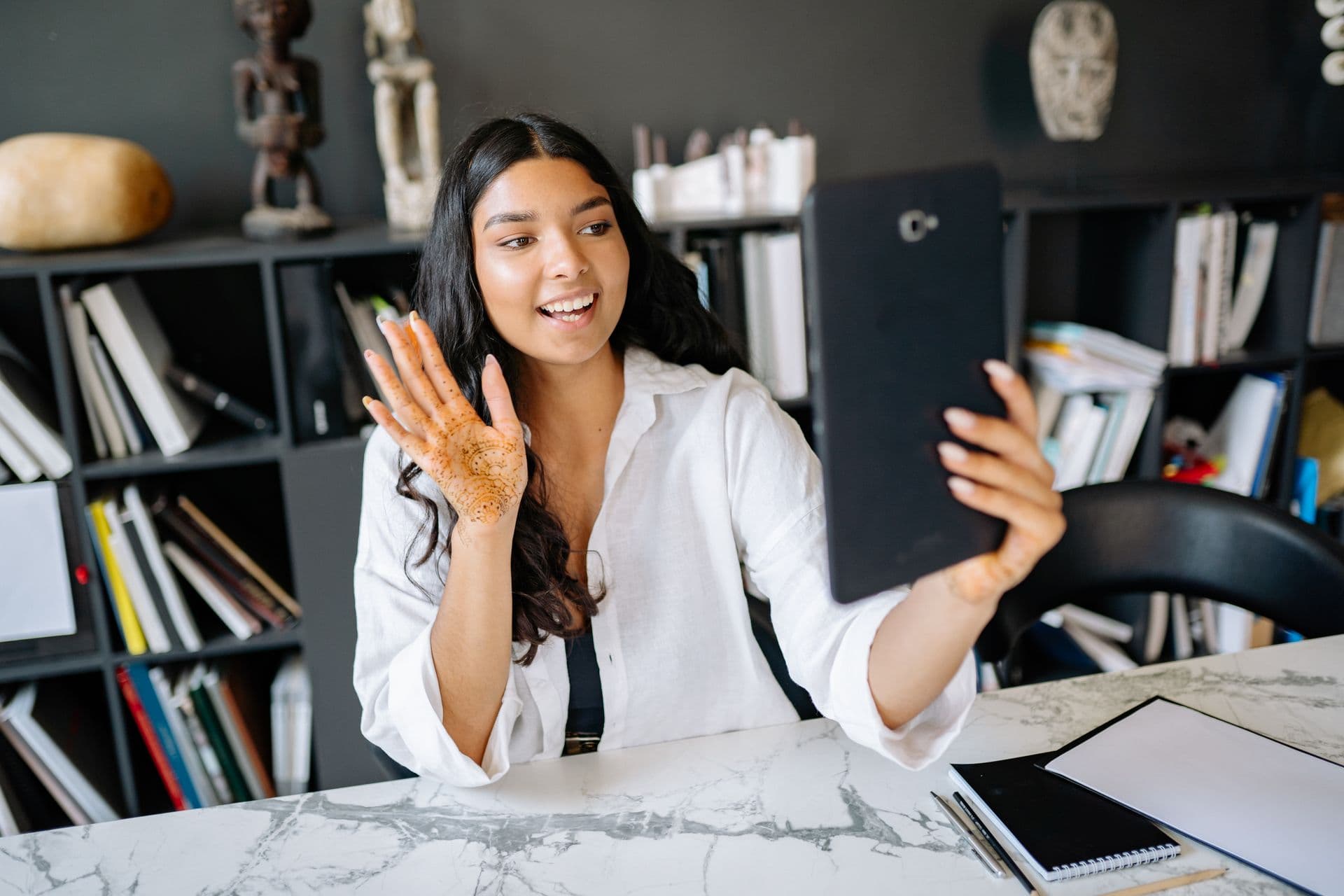 Young woman with henna on her hand waves at a tablet held up at her desk