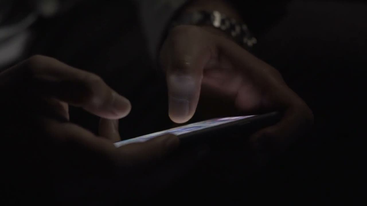 Hands holding a smartphone in darkness, fingertip lit by the glowing screen