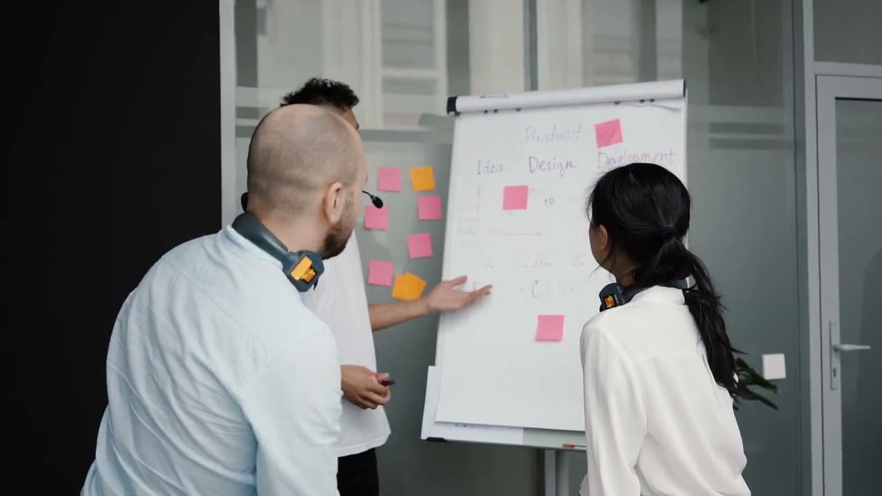 Three coworkers at a flip chart with pink and orange sticky notes, planning a product