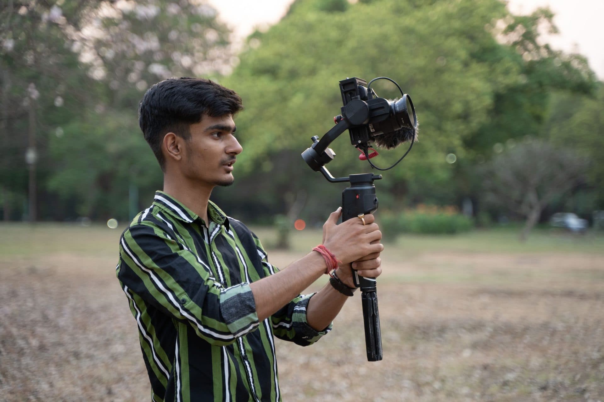 Young man in a striped shirt films with a gimbal-mounted camera in a park