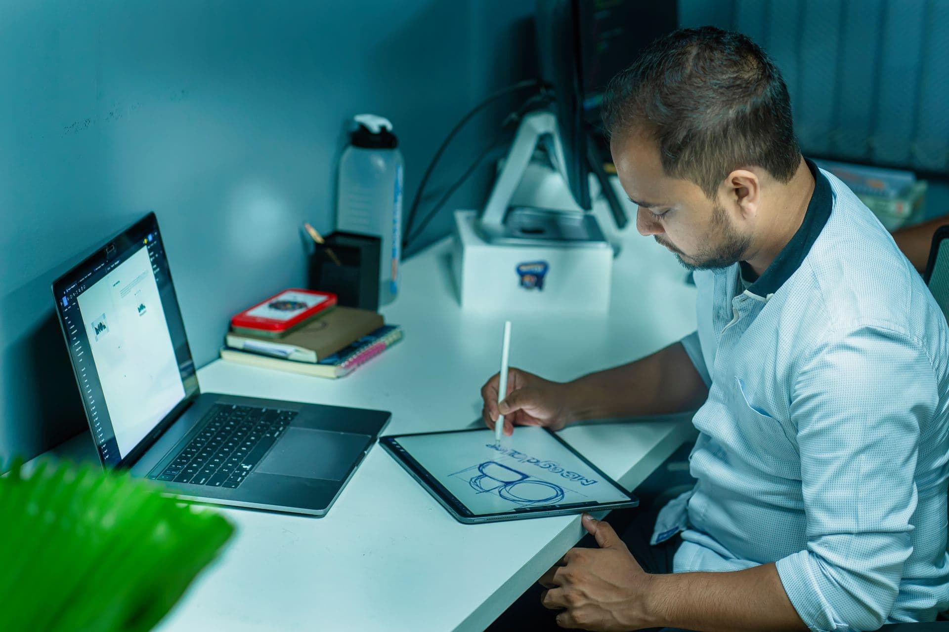 Web designer sketching a layout on a tablet with a stylus beside an open laptop