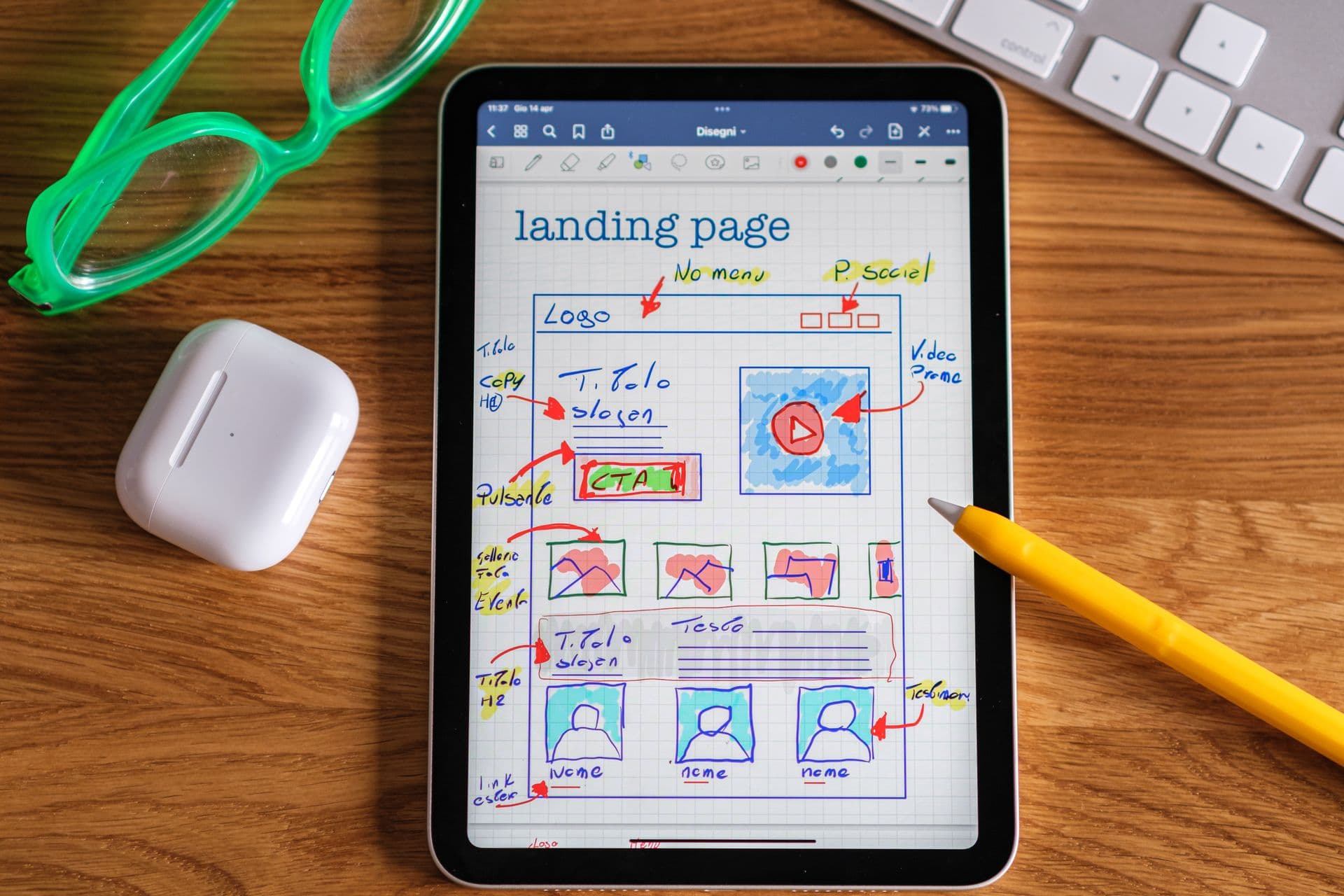 Hand-drawn landing page wireframe on a tablet, with a stylus and glasses on a wooden desk