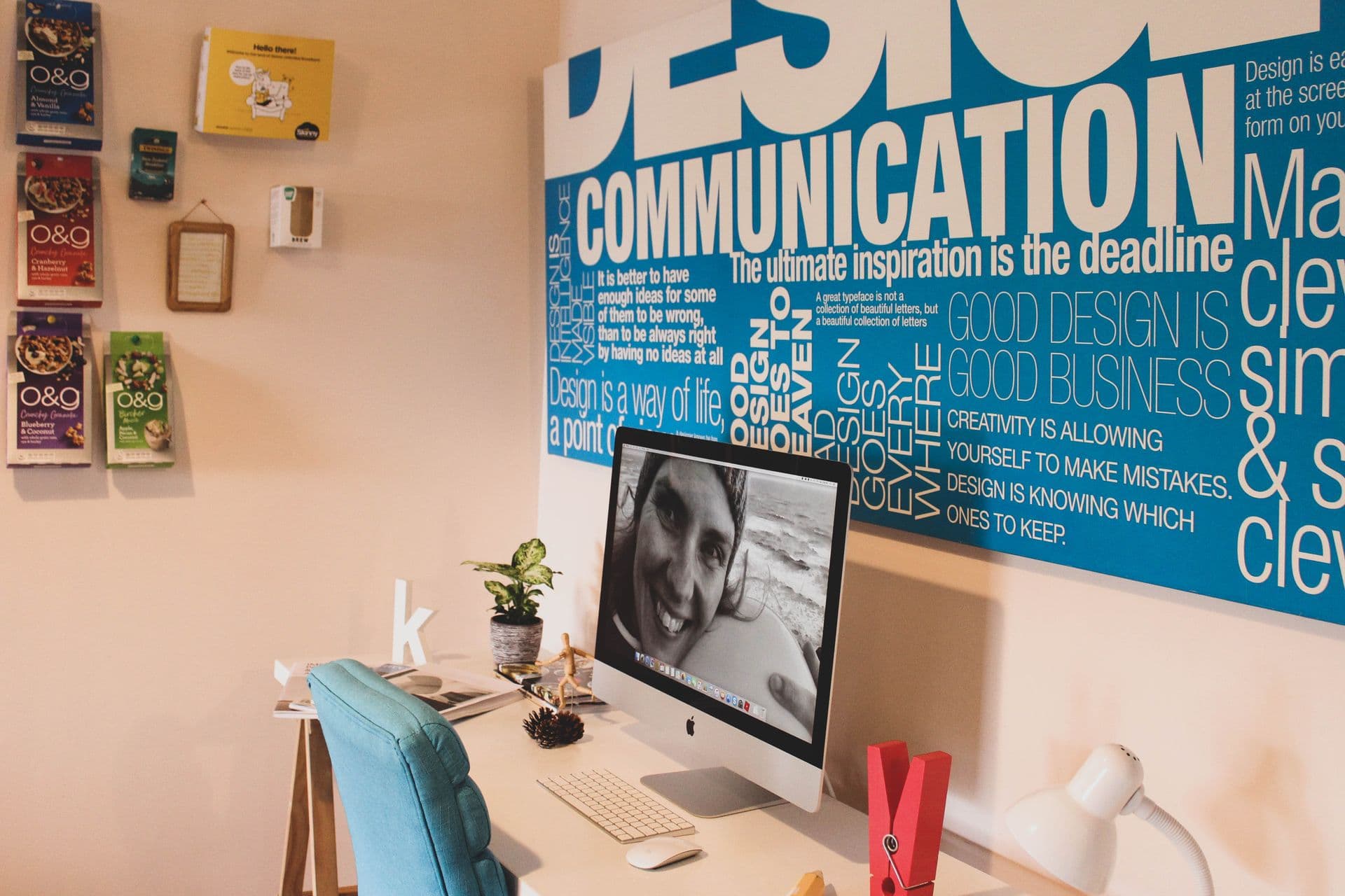 Design studio desk with a desktop computer beneath a large blue typography wall poster