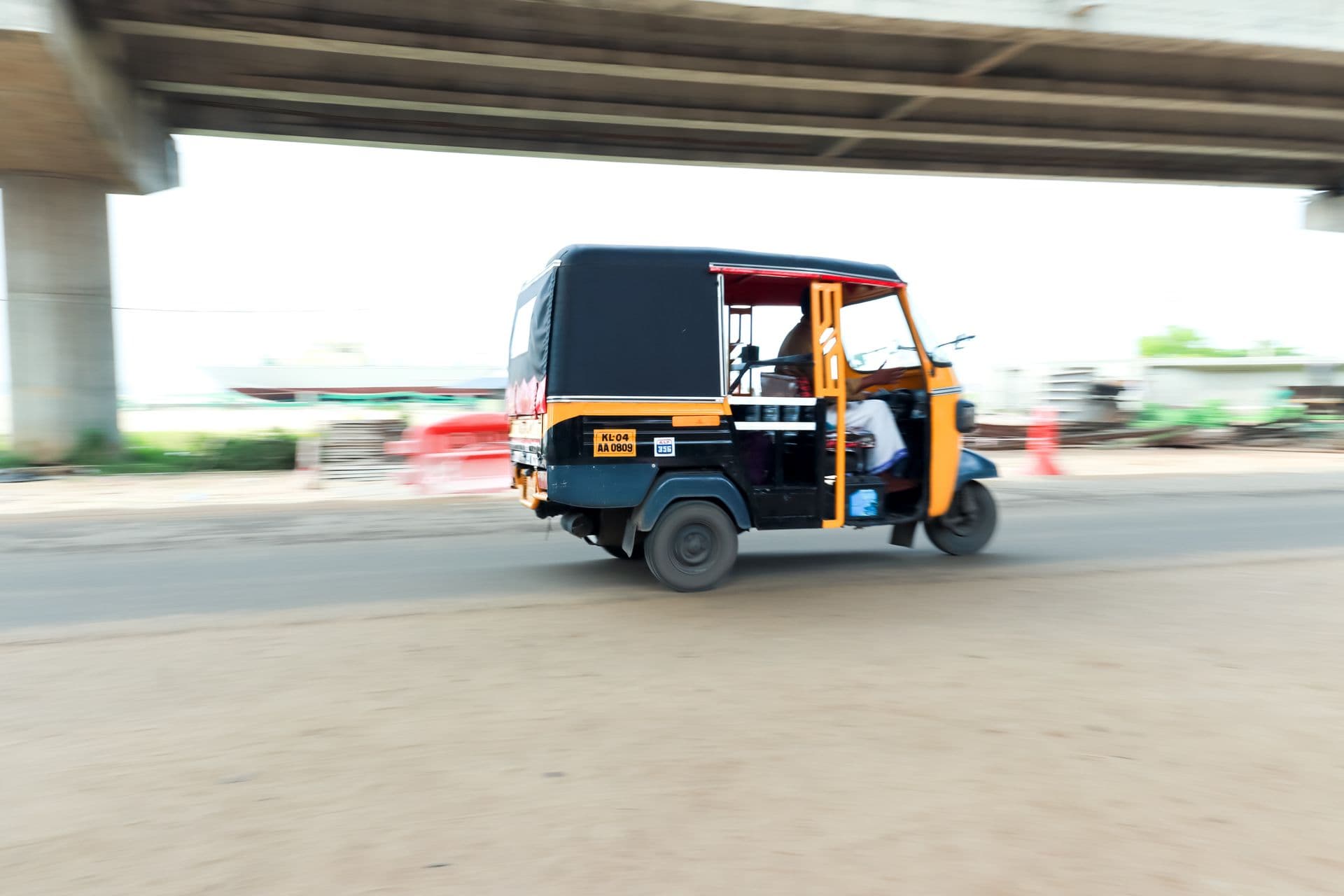 Black and yellow auto rickshaw speeding beneath an elevated highway, captured with panning motion blur