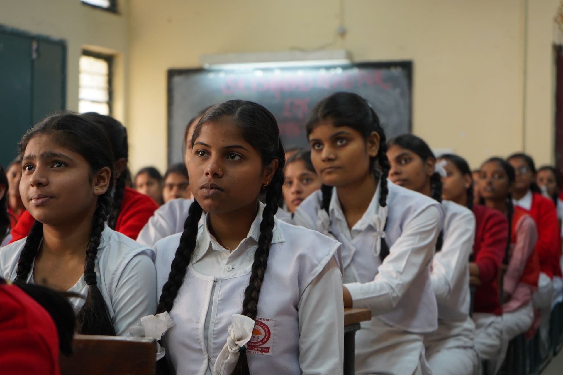 Indian schoolgirls in white uniforms with braided hair listening attentively in a classroom