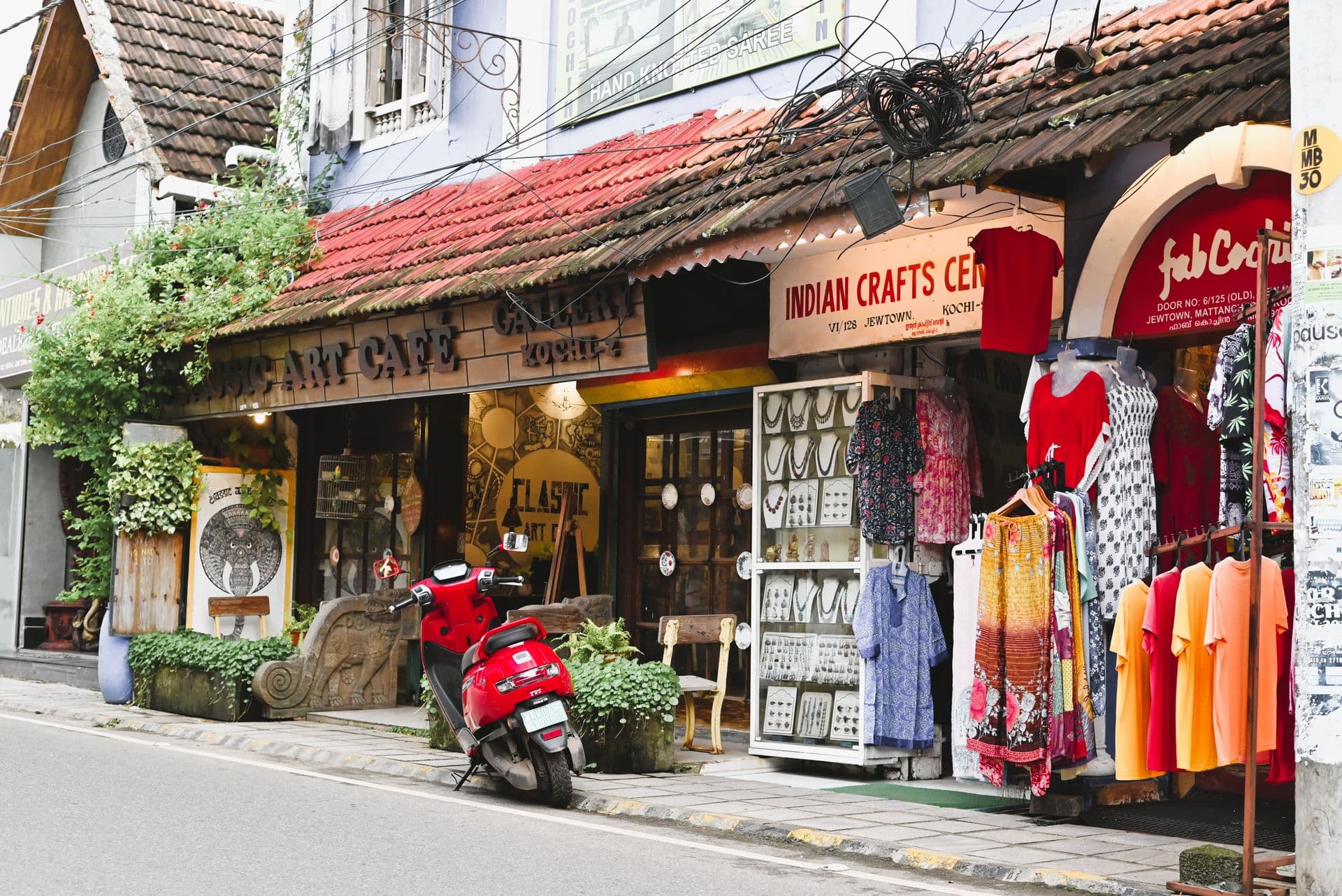 Craft shops and clothing racks beneath tiled roofs on a Jew Town street in Kochi