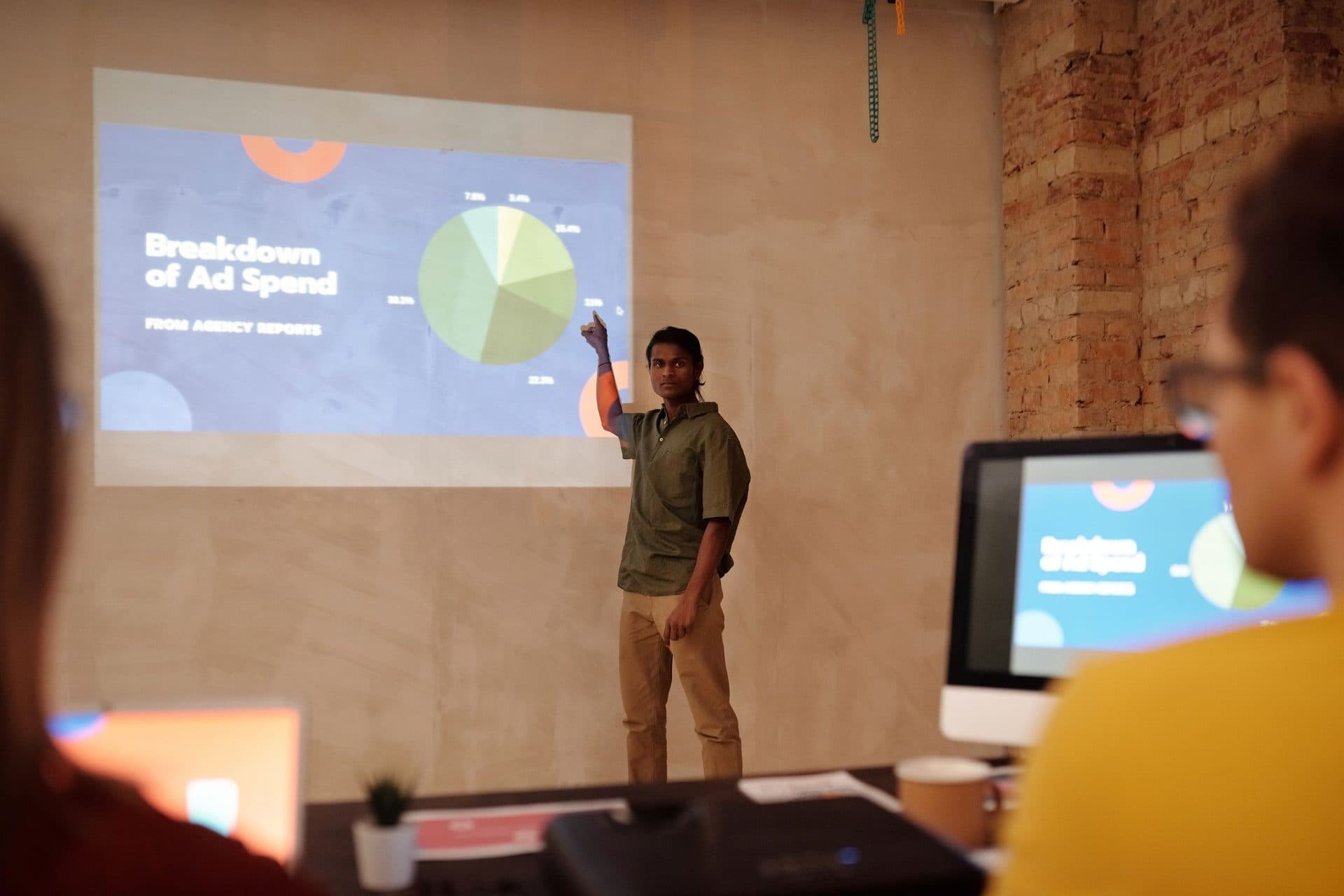 Young man presents a projected slide titled Breakdown of Ad Spend with a pie chart