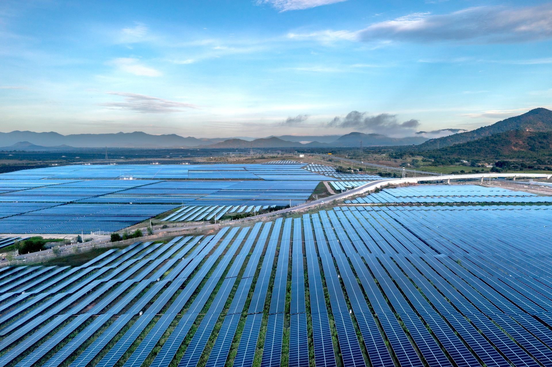 Aerial view of a vast solar farm with rows of panels stretching toward hills