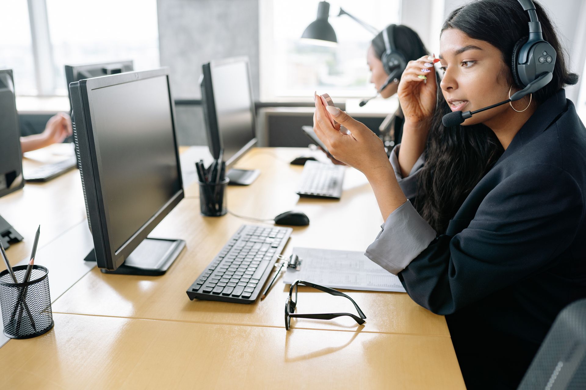 Woman wearing a headset gestures while speaking at a desk lined with monitors
