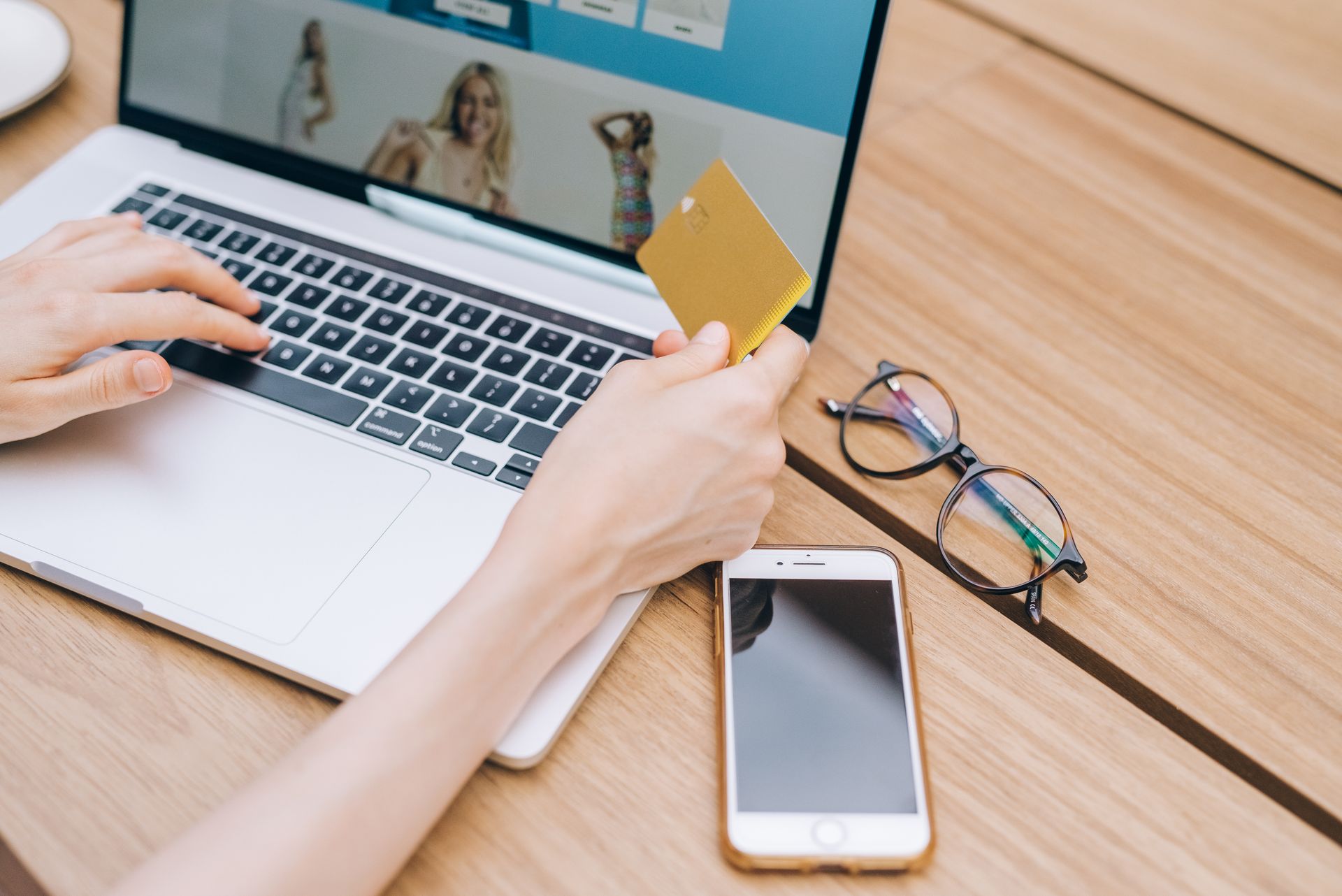 Hands on a laptop holding a gold payment card next to a smartphone